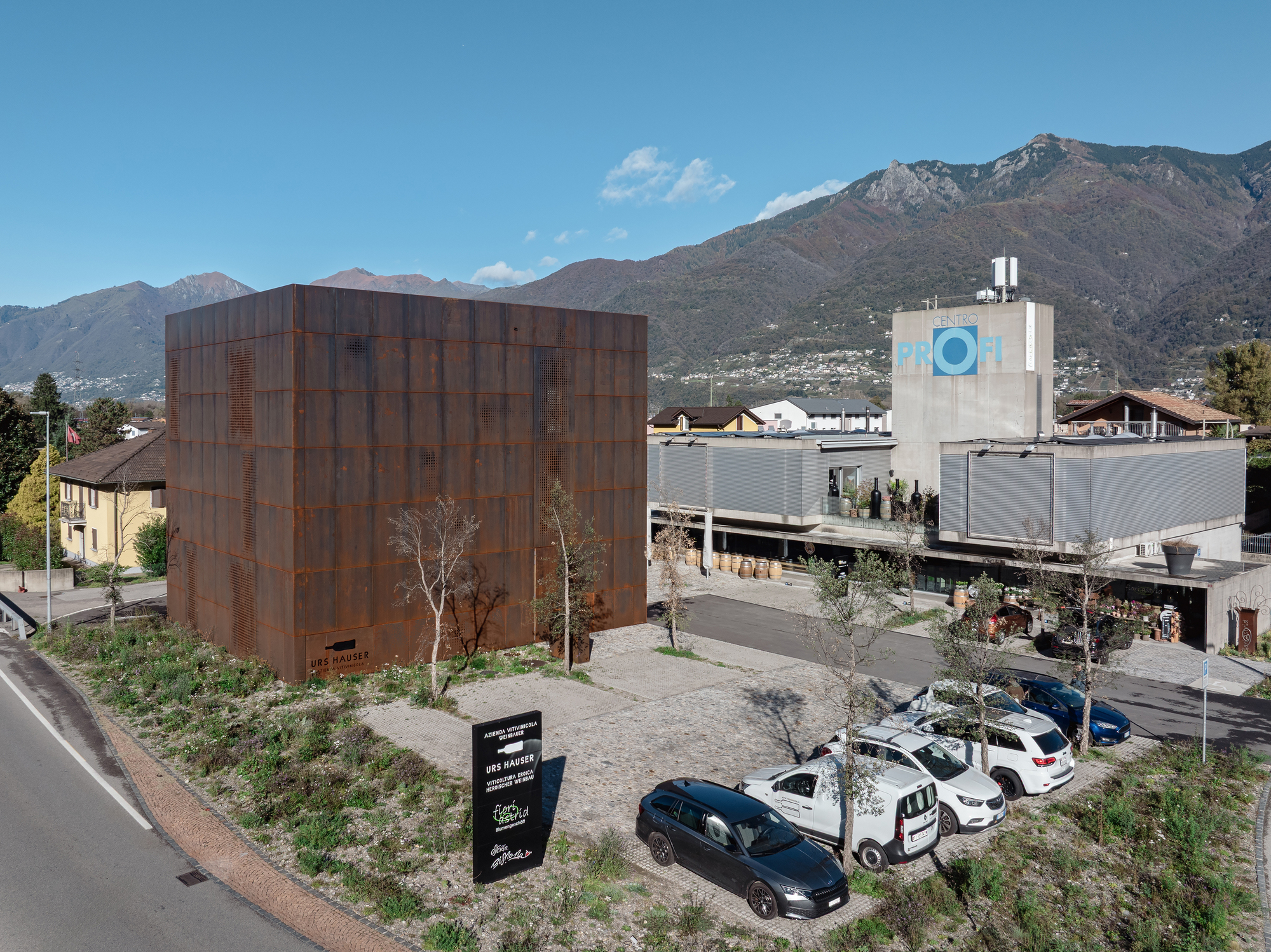 Weathered steel paneled cube adjacent to industrial buildings with mountains in the background