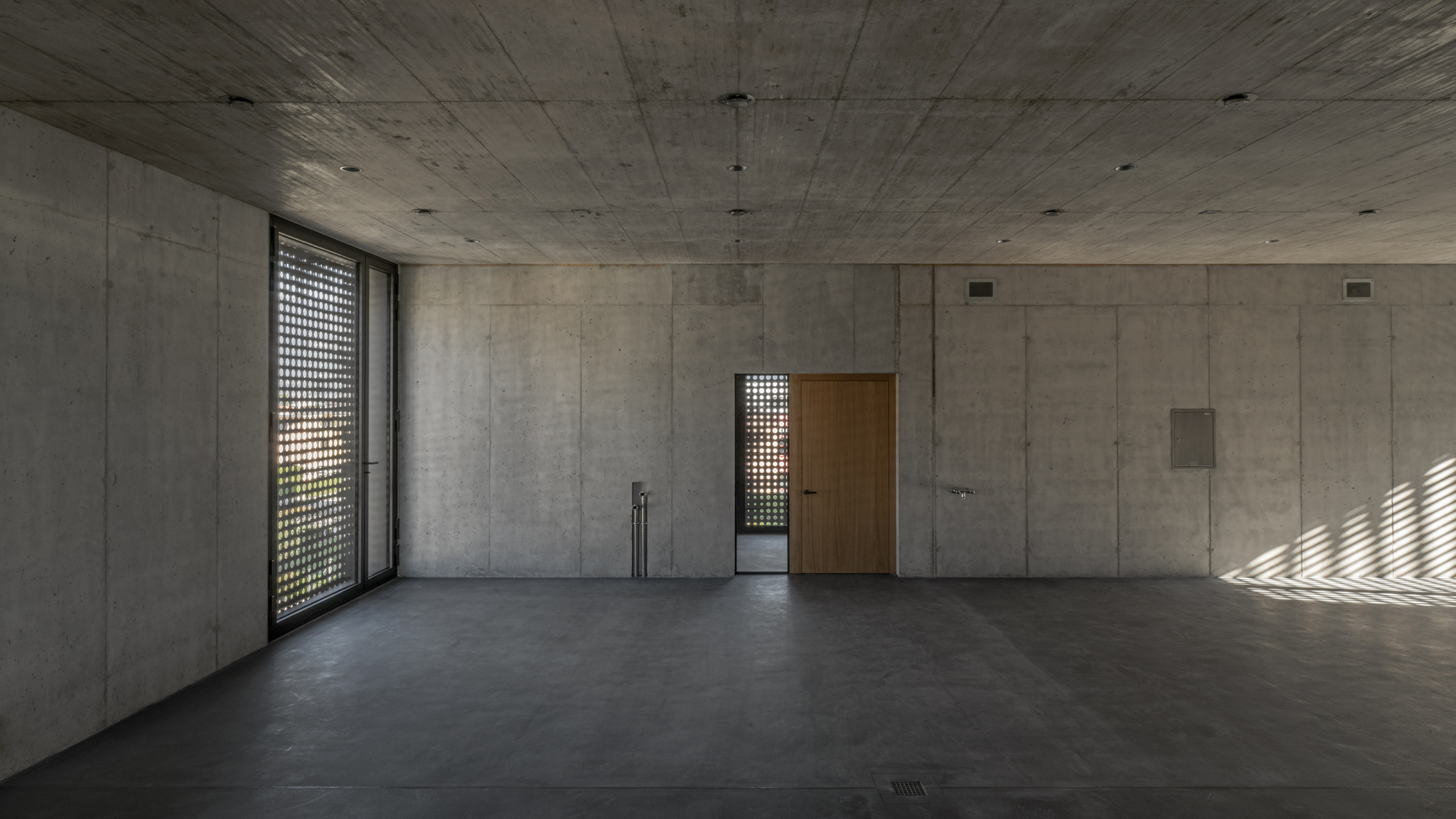 Bare concrete interior space with perforated screen window casting dappled light on the floor