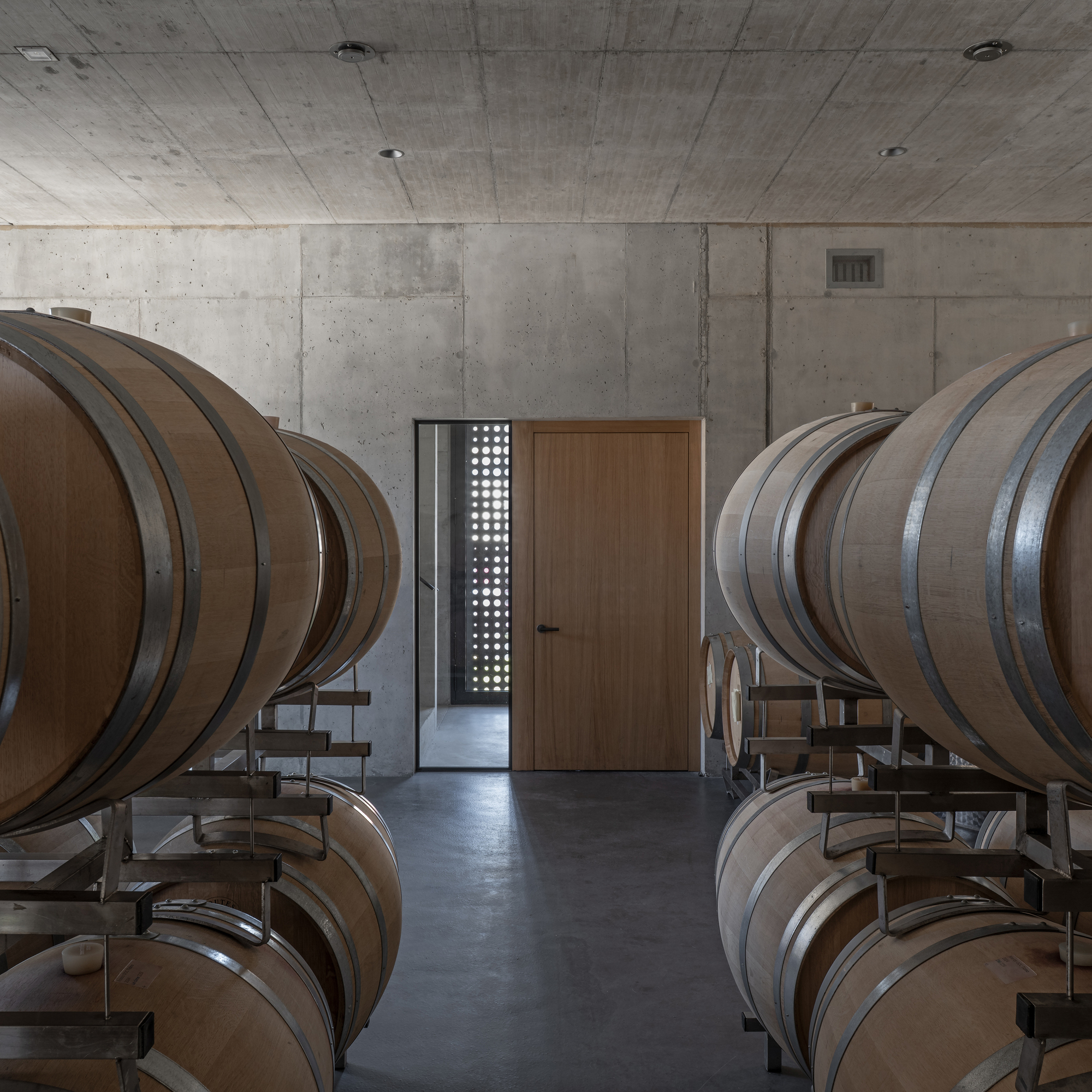 Symmetrical view of oak barrel rows flanking a timber door with a perforated screen beyond