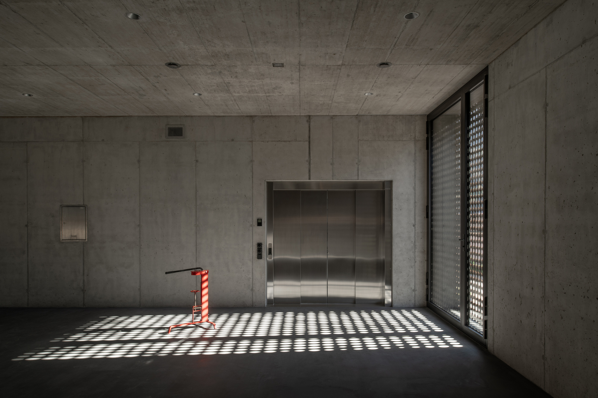 Concrete lobby with stainless steel elevator doors and patterned light from a perforated screen window