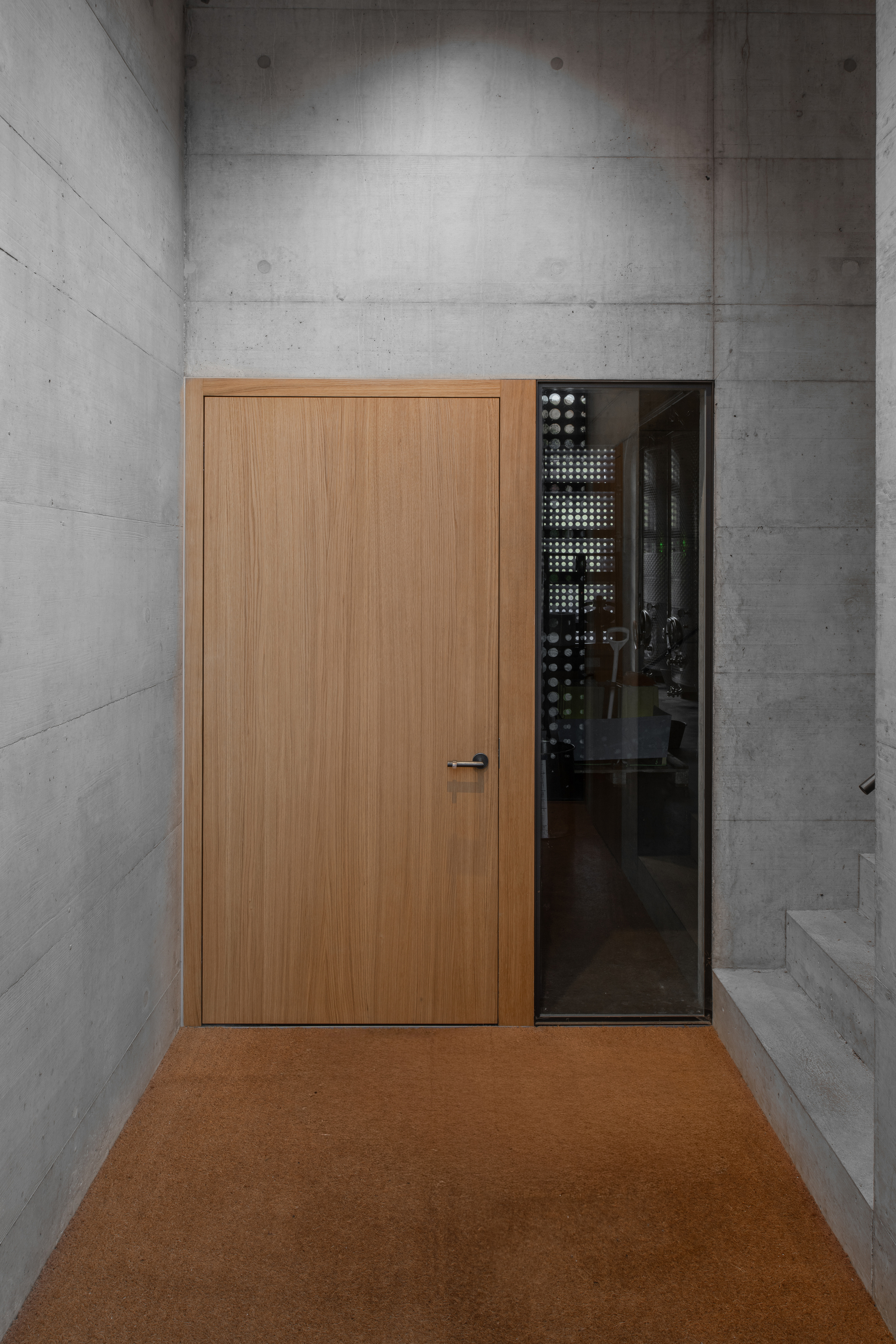 Timber door and glass panel set into board-formed concrete walls above cork flooring