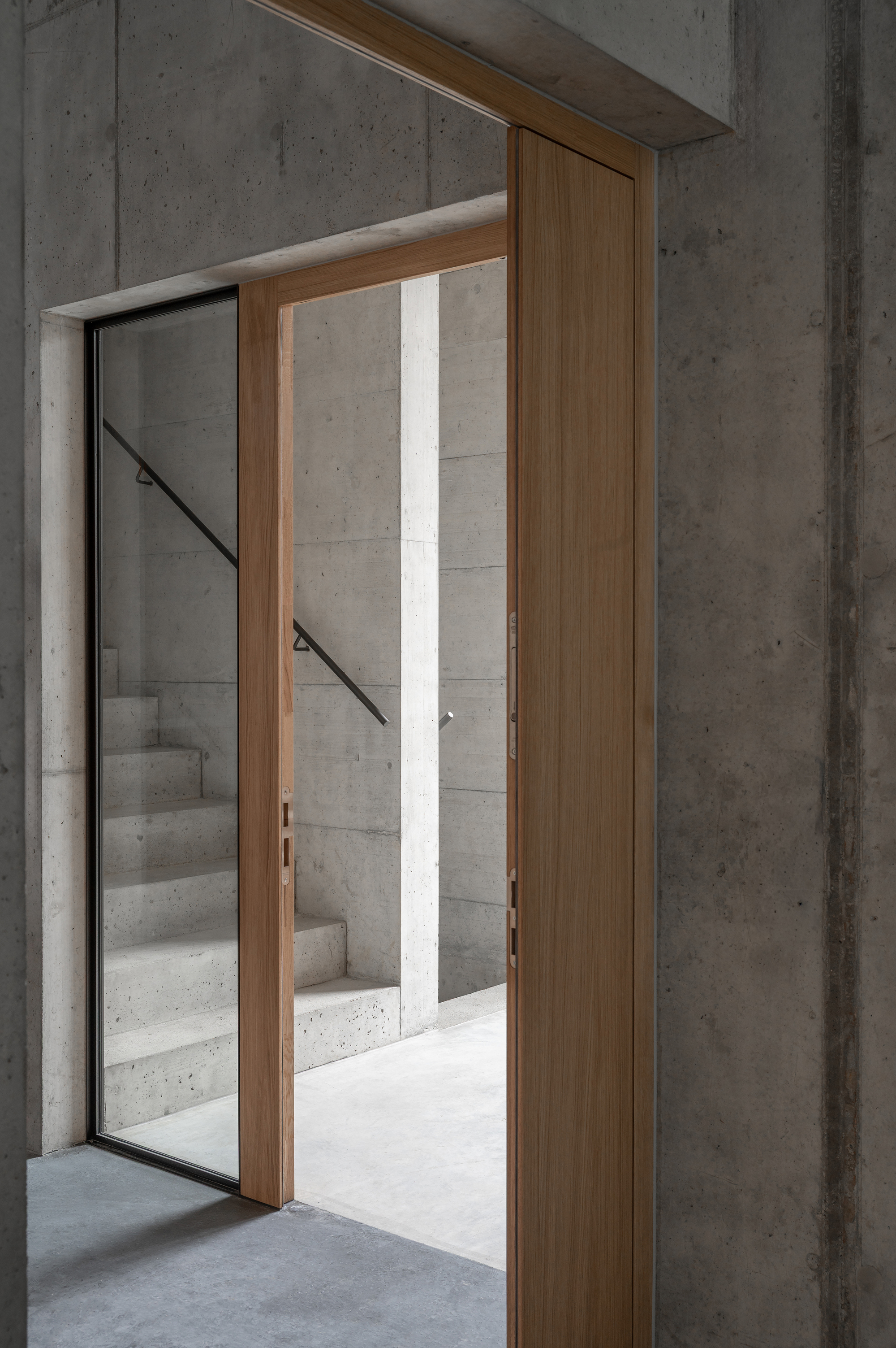 Timber-framed doorway opening to a concrete staircase with metal handrail in daylight