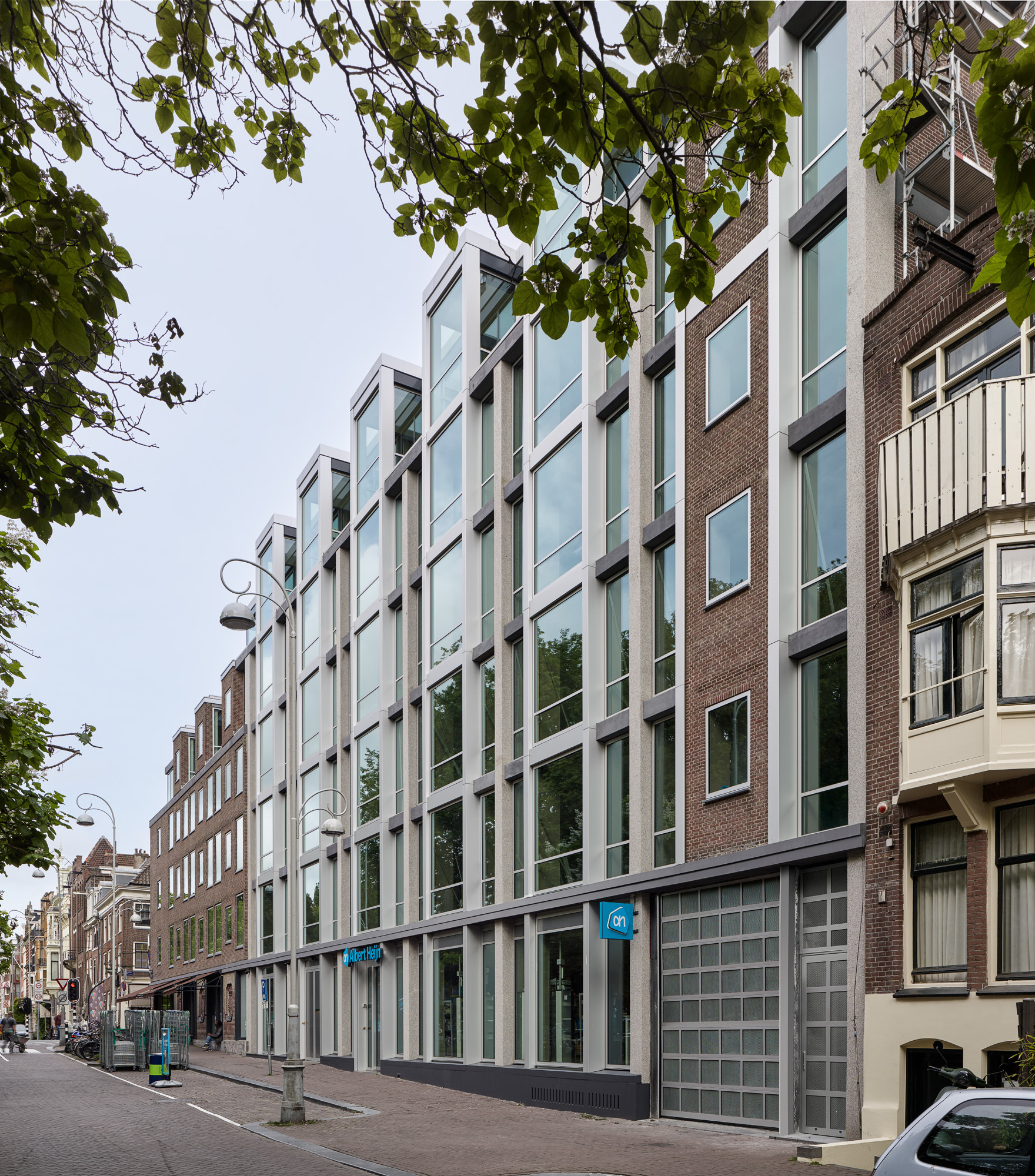 Facade showing alternating bands of pale brick and glazed panels framed by tree branches