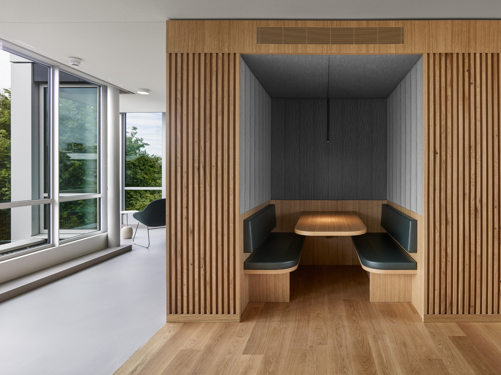 Timber-slatted booth with built-in banquette seating and table beside a white corridor with exterior views
