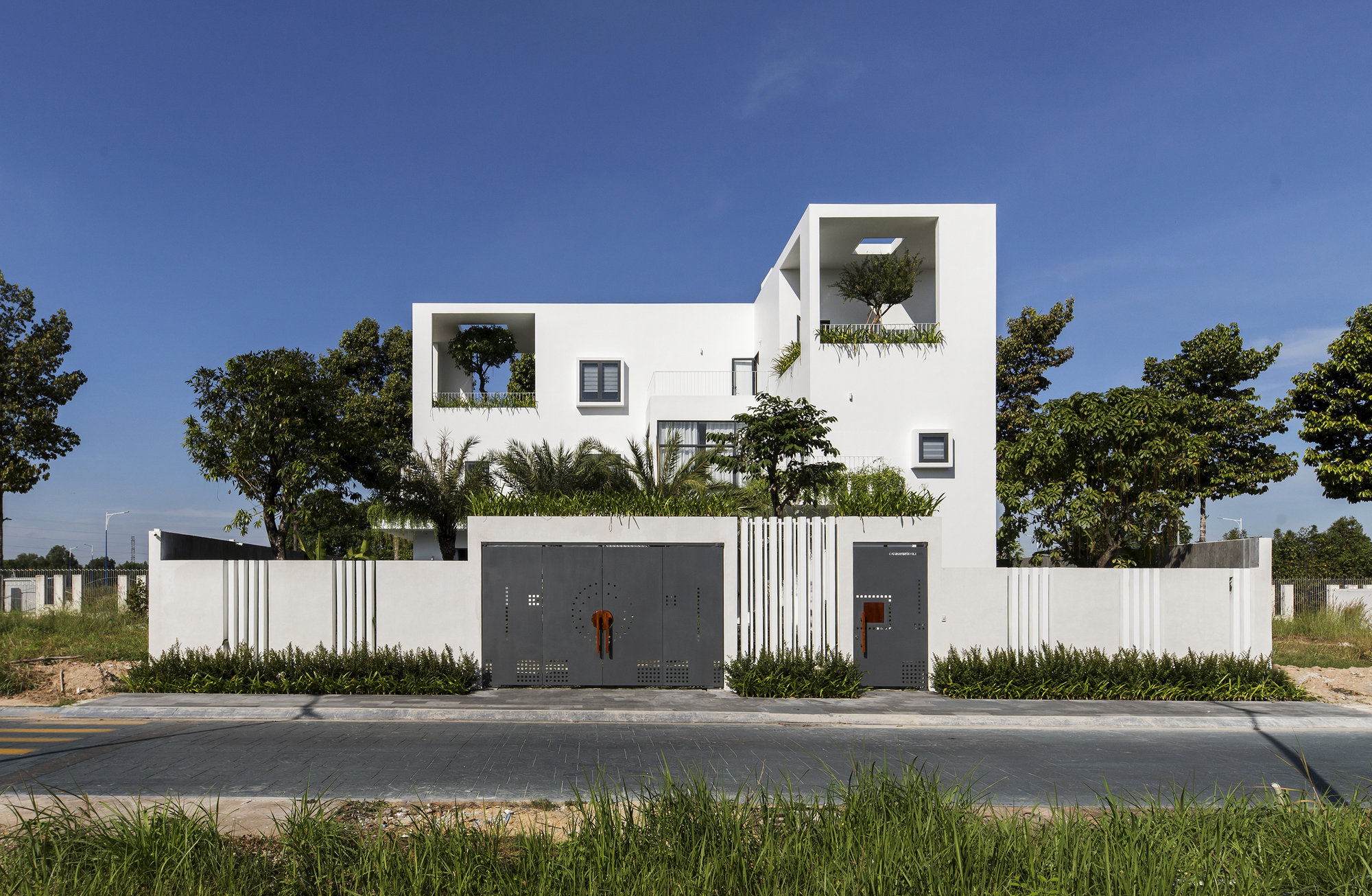 Street view of white facade with stacked planted terraces behind vertical slat boundary wall