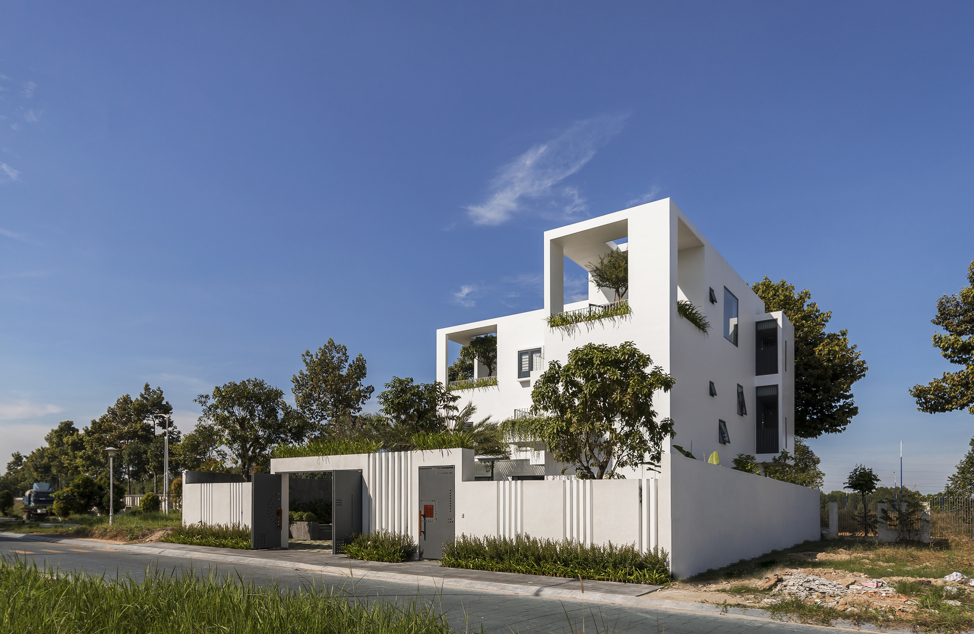 Corner view of the stepped white volumes with planted balconies and perimeter fence
