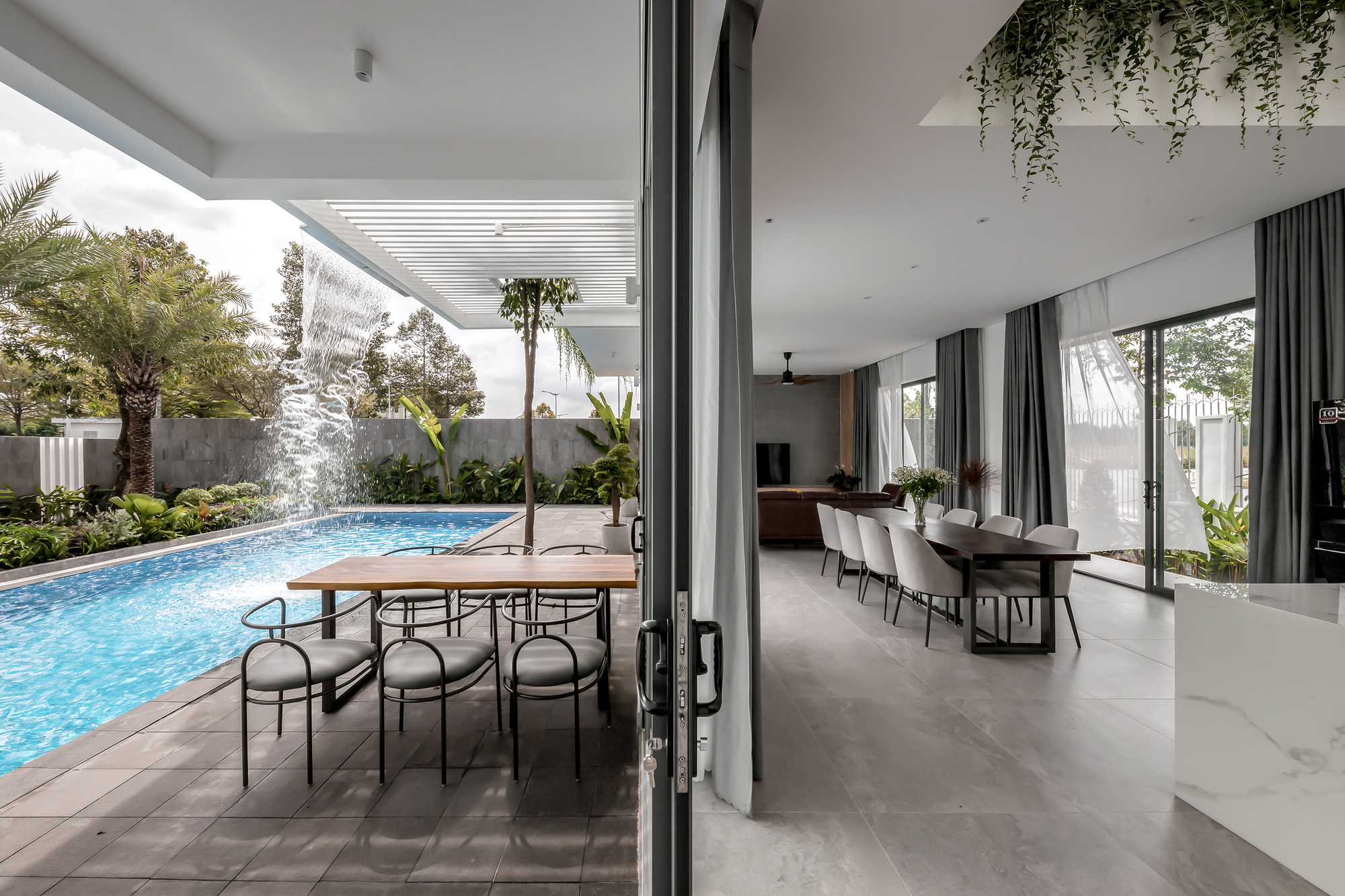 Open dining area with floor-to-ceiling glass doors connecting to a covered poolside terrace with slatted pergola