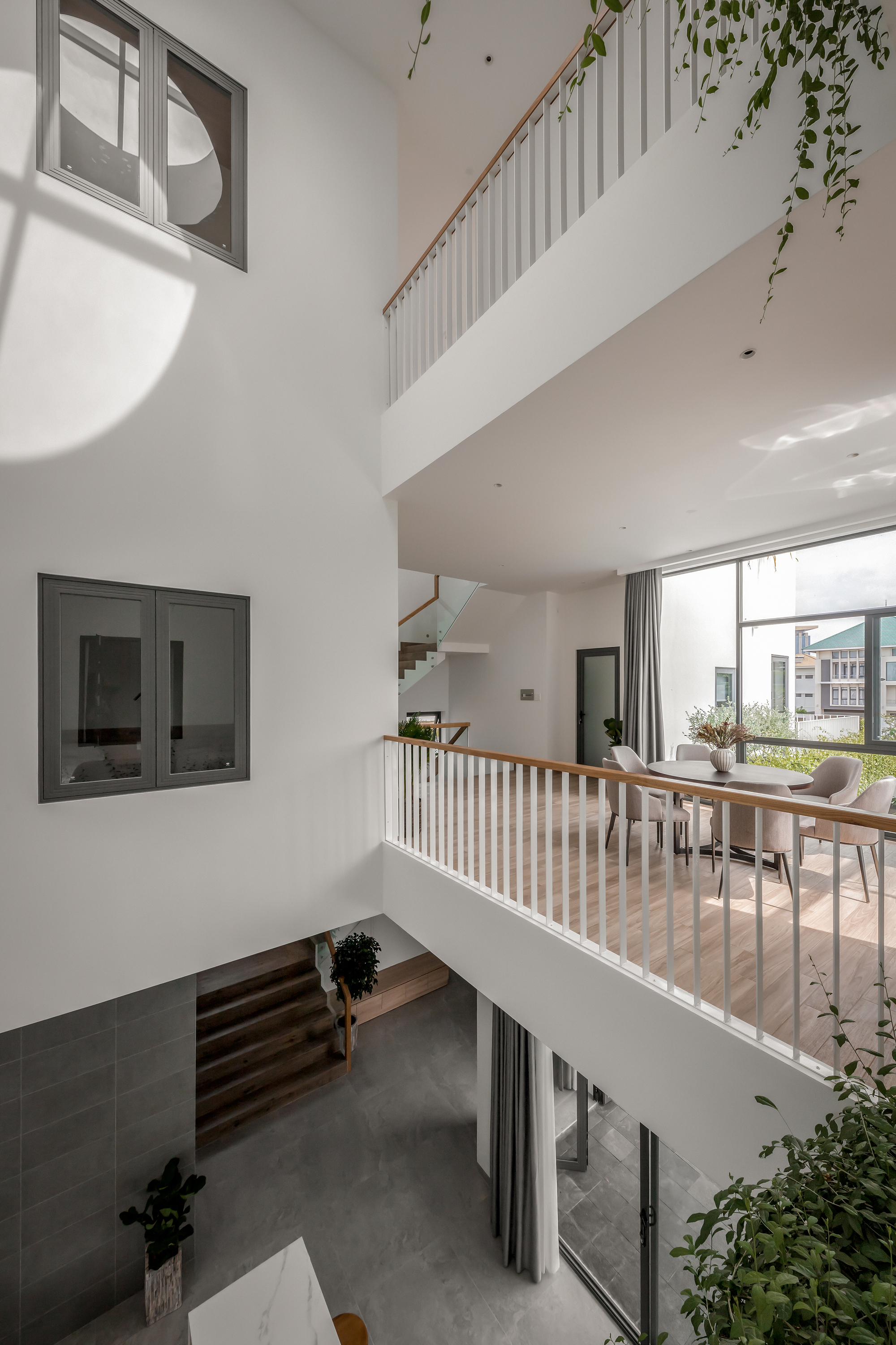 Triple-height void with timber-railed bridges linking levels and windows puncturing white walls in morning light
