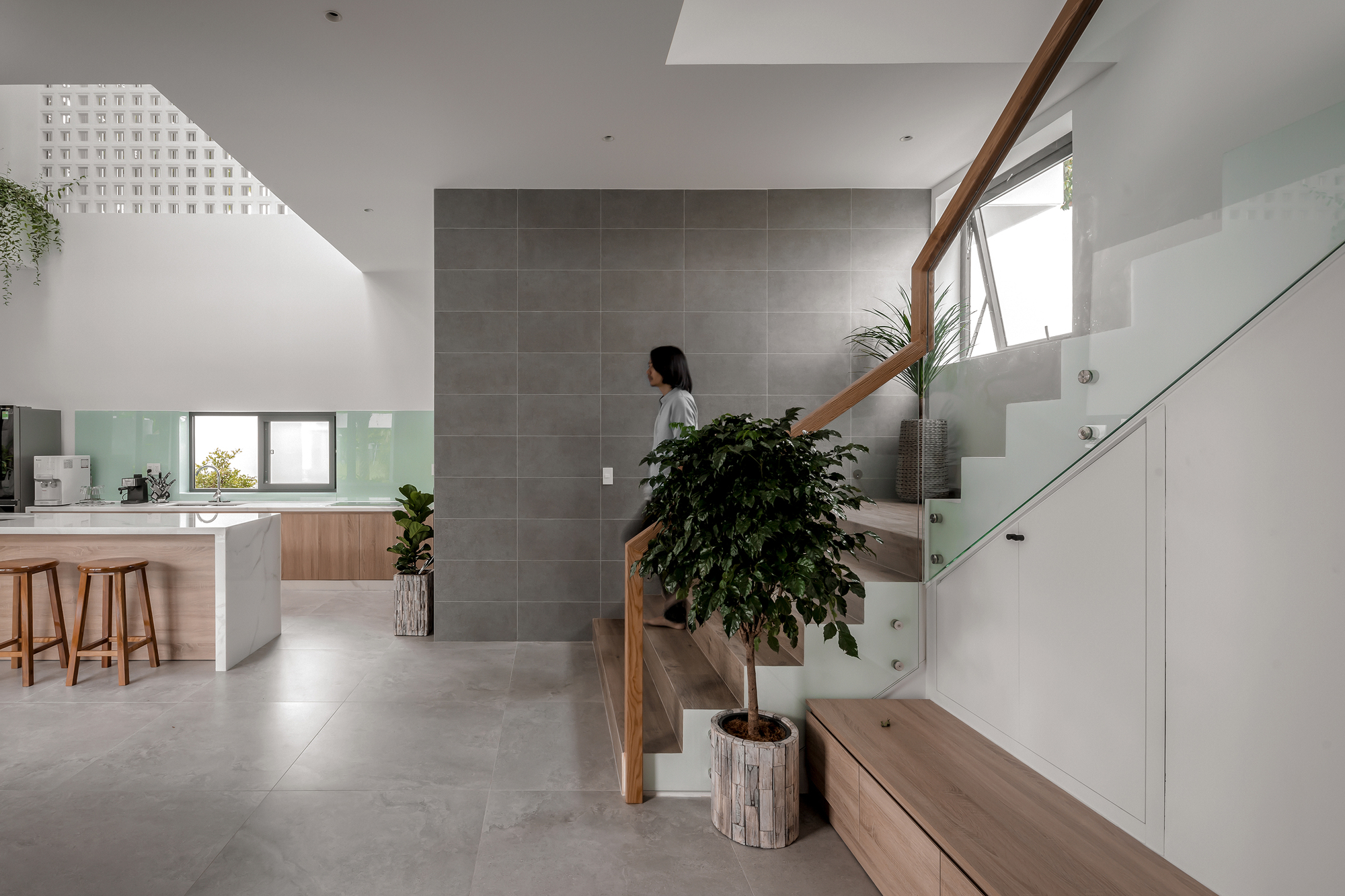 Grey tiled feature wall anchoring an open stairwell lit by a perforated skylight above
