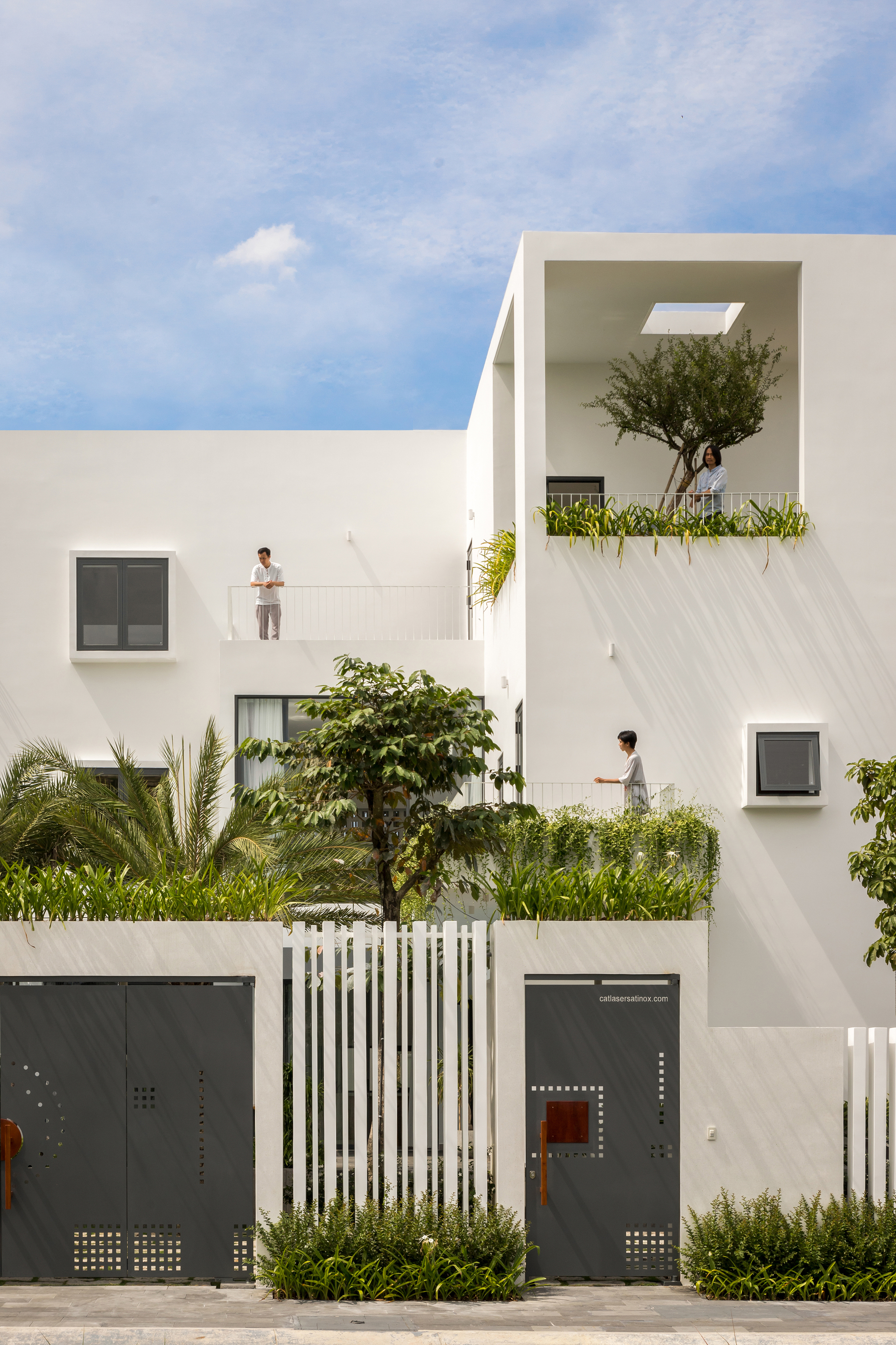 Street facade showing white volumes with recessed balconies and residents on upper terraces
