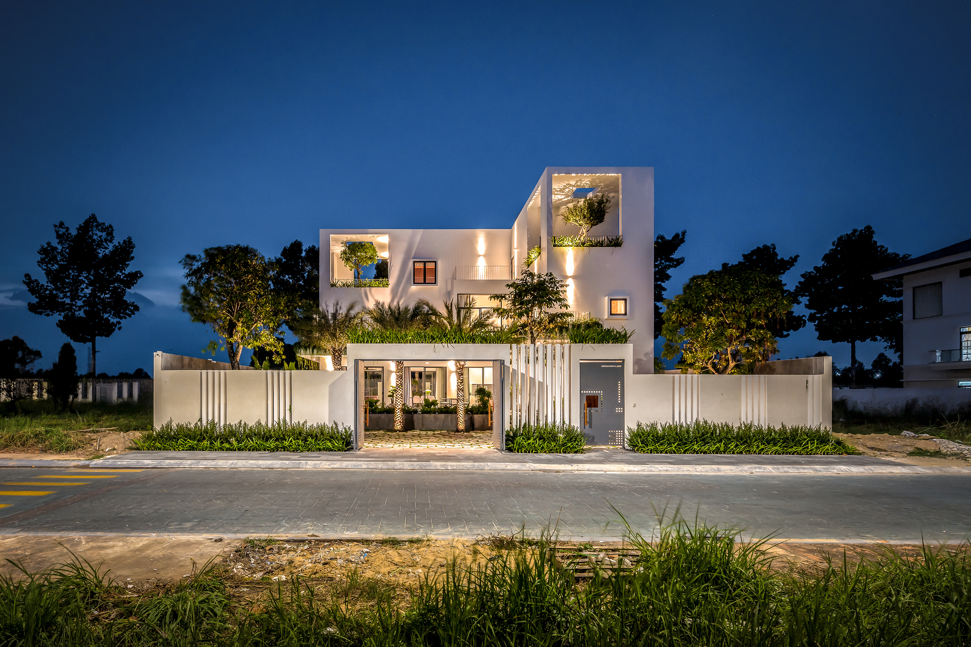 Front elevation at dusk with illuminated interior courtyard and planted perimeter wall