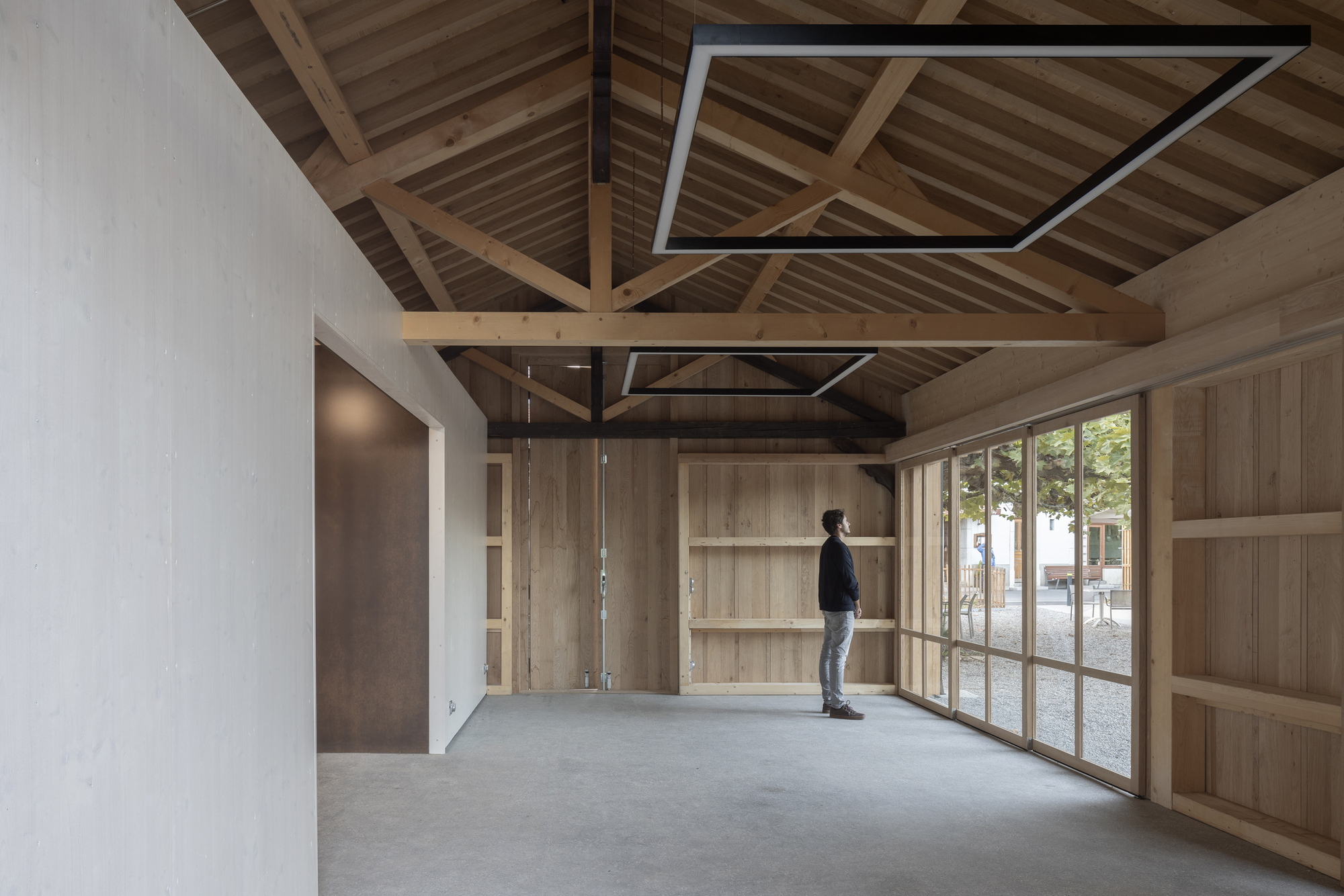 Interior space with exposed timber truss ceiling and a figure standing by glazed doors