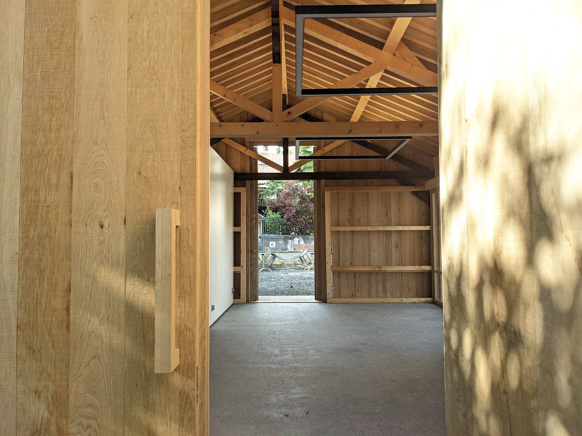 View through timber doorway toward the exposed roof structure with dappled light on plywood walls