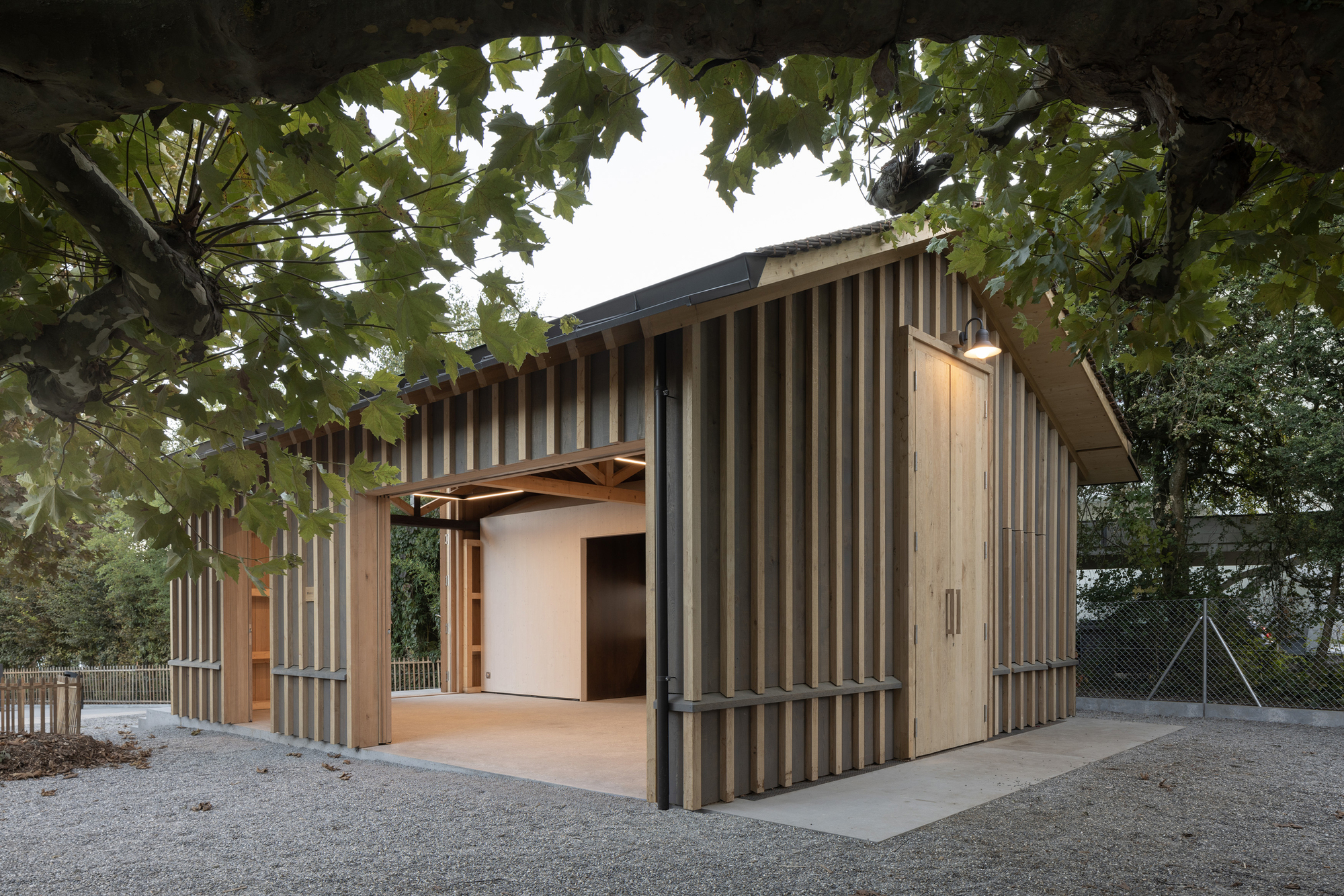 Low pavilion with alternating grey and timber vertical cladding beneath mature trees in autumn