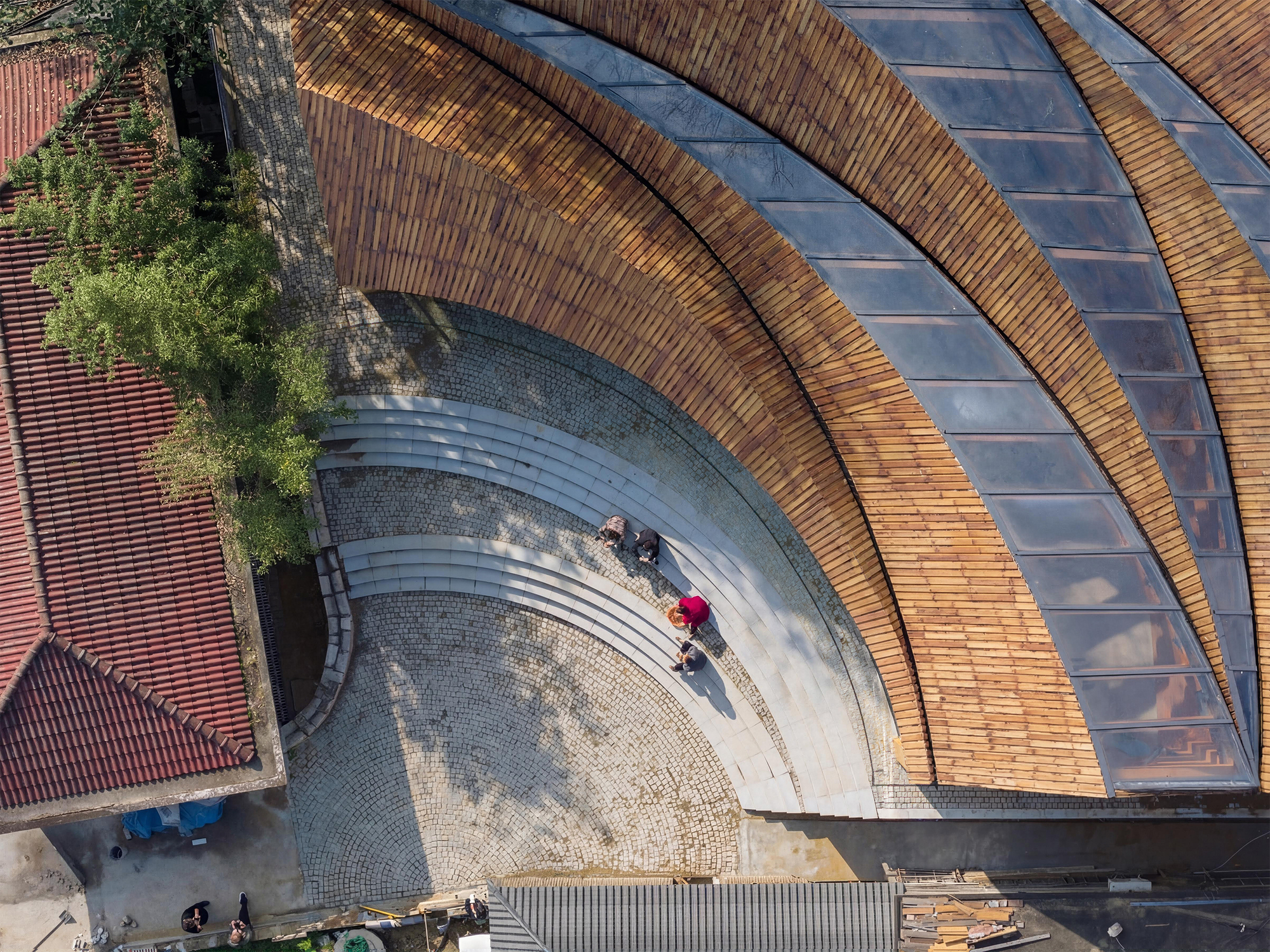 Aerial view of the curving timber roof with skylights and stone-paved plaza below