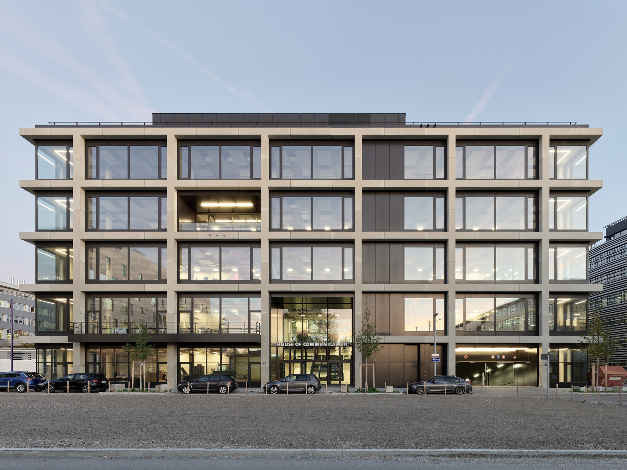 Street-facing facade with precast concrete grid framing floor-to-ceiling windows under an overcast sky