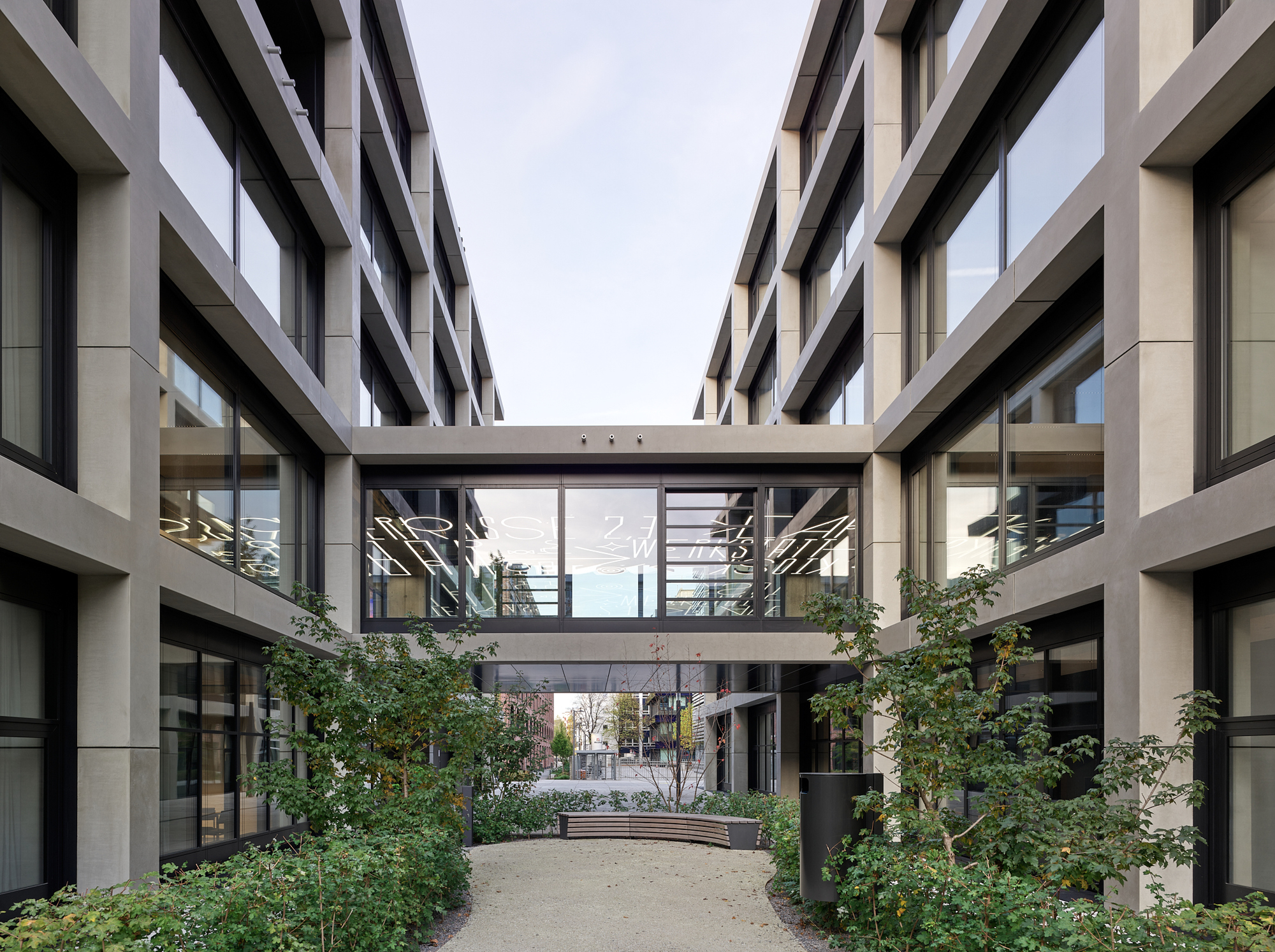 Landscaped courtyard with planted beds and trees beneath two cantilevered glass bridges connecting the wings