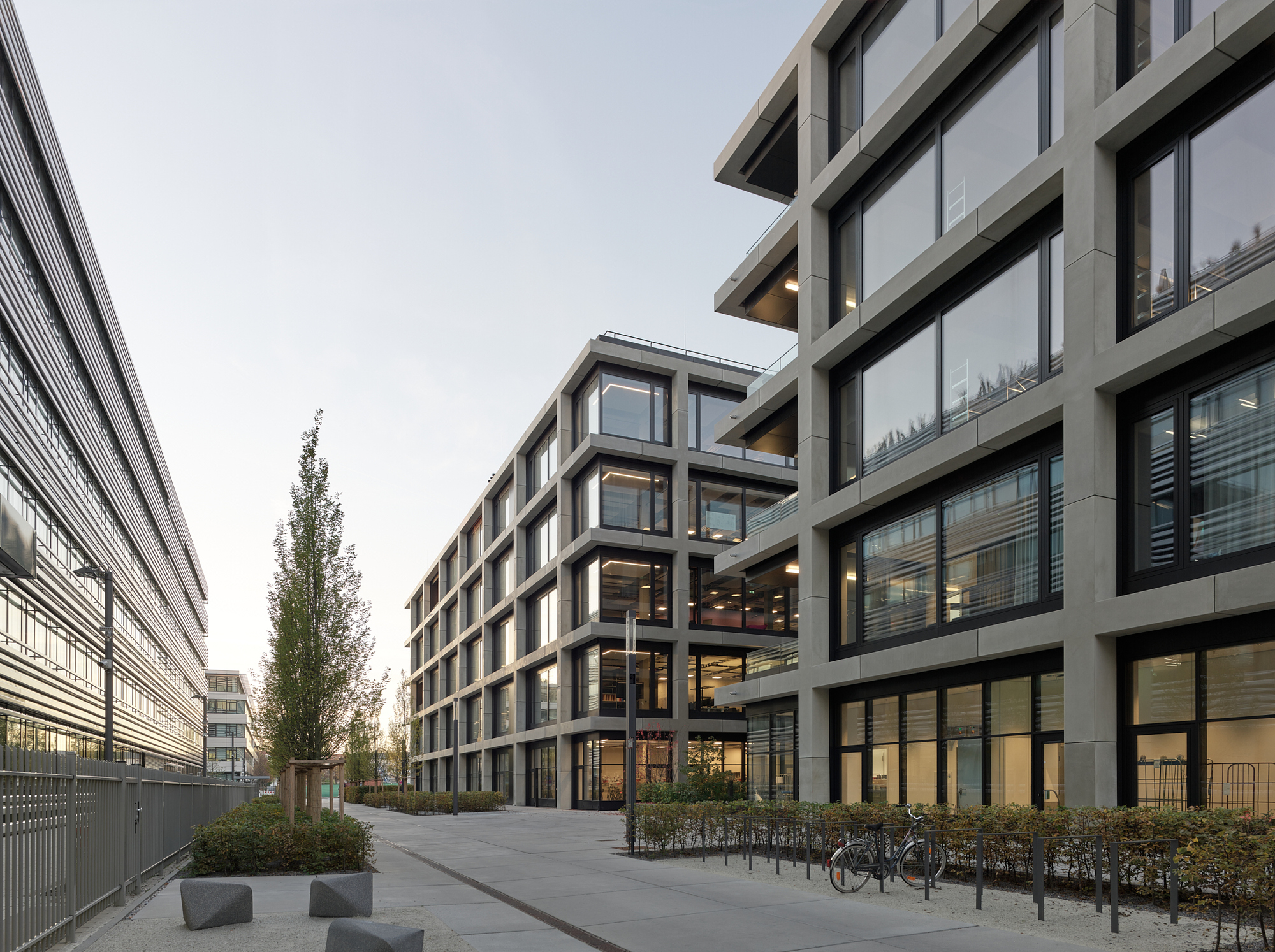 Courtyard view at dusk showing the gridded facade with interior lights glowing and bicycles parked below
