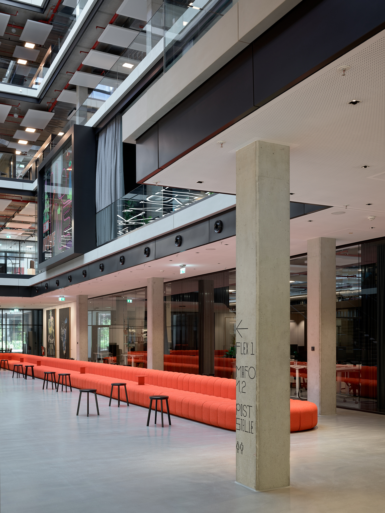 Interior atrium with long orange upholstered bench seating and exposed concrete column in the foreground