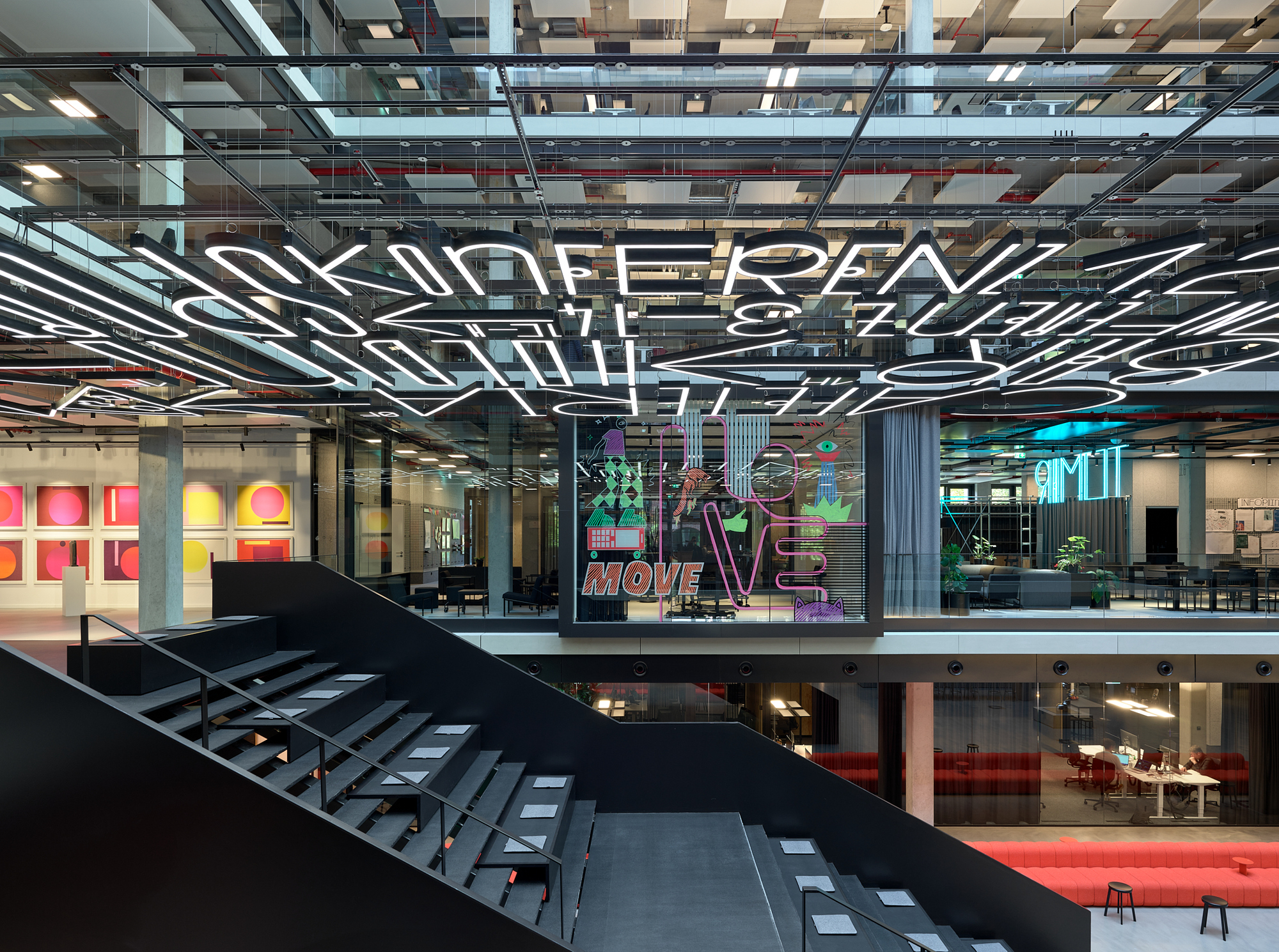Multi-level atrium with black steel staircase and glazed offices featuring neon signage on upper floors
