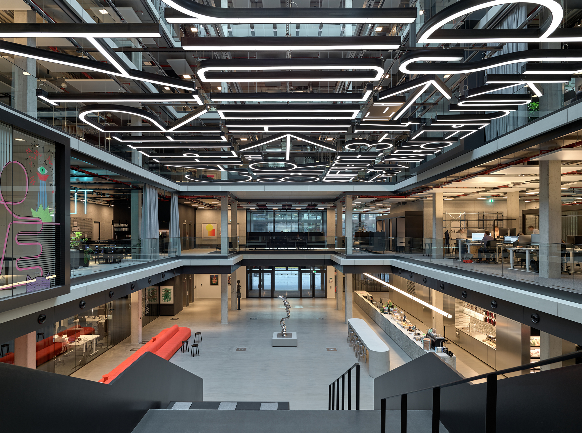 Multi-story atrium with graphic white light fixtures suspended above open office floors and a central void