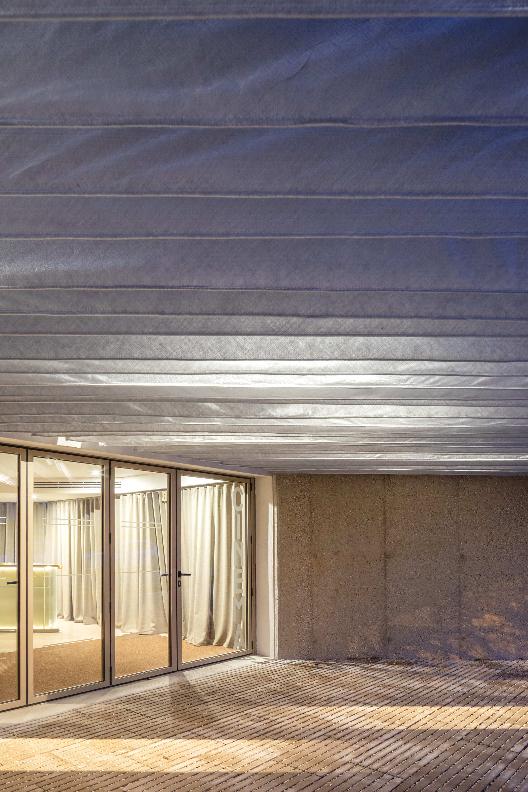 Night view of the folded canopy ceiling reflecting light above glass doors and concrete wall
