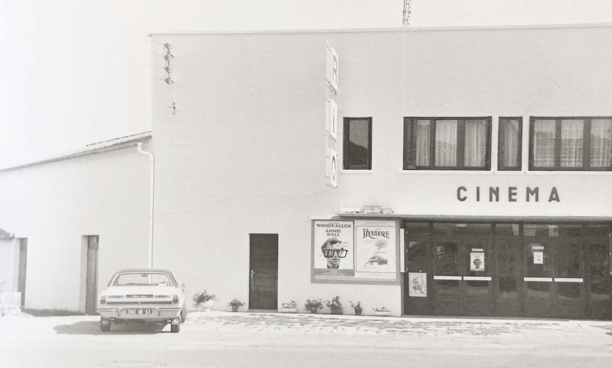 White stucco cinema facade with rectangular windows and a parked car in front