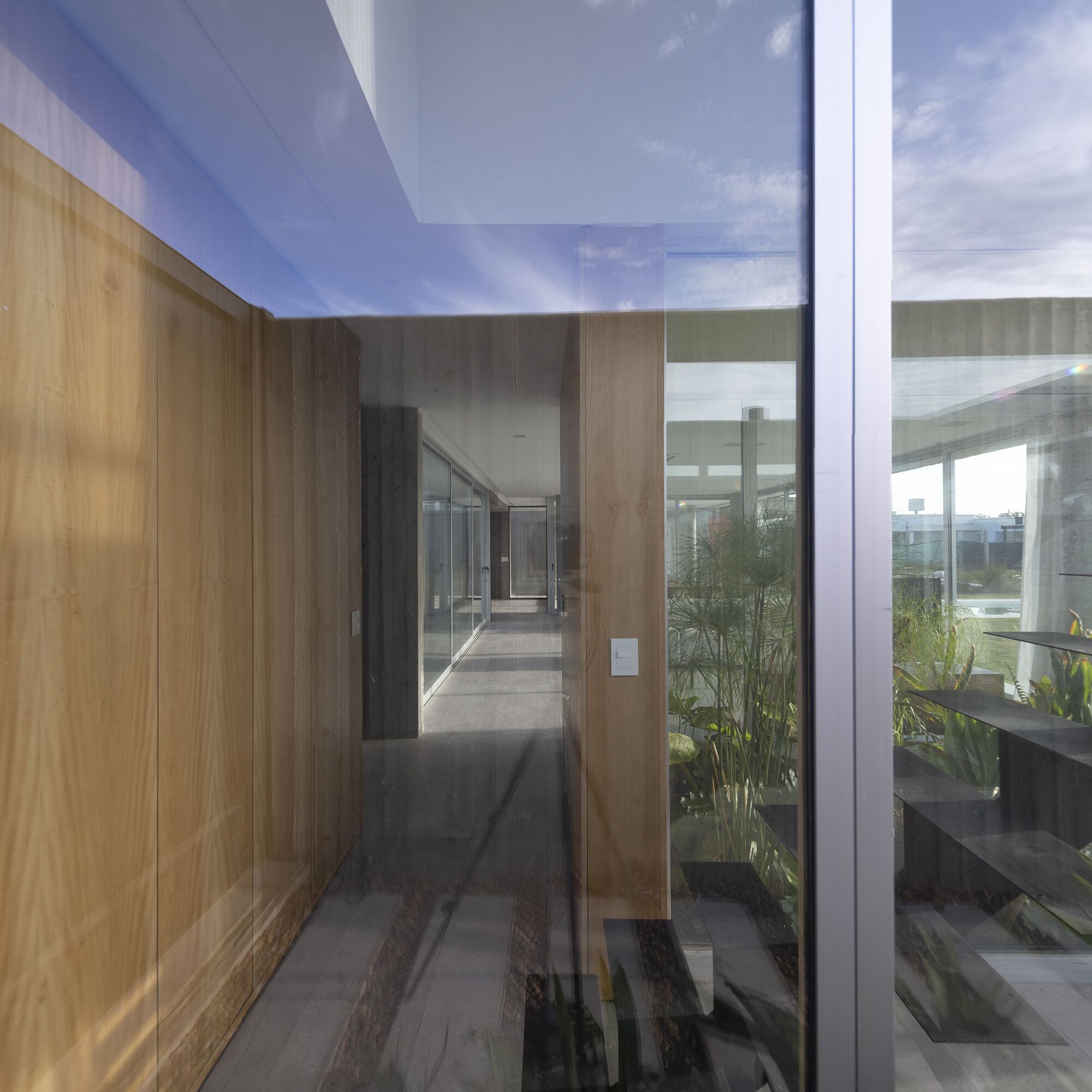 Glass-walled corridor with timber-paneled walls and reflections of courtyard plantings
