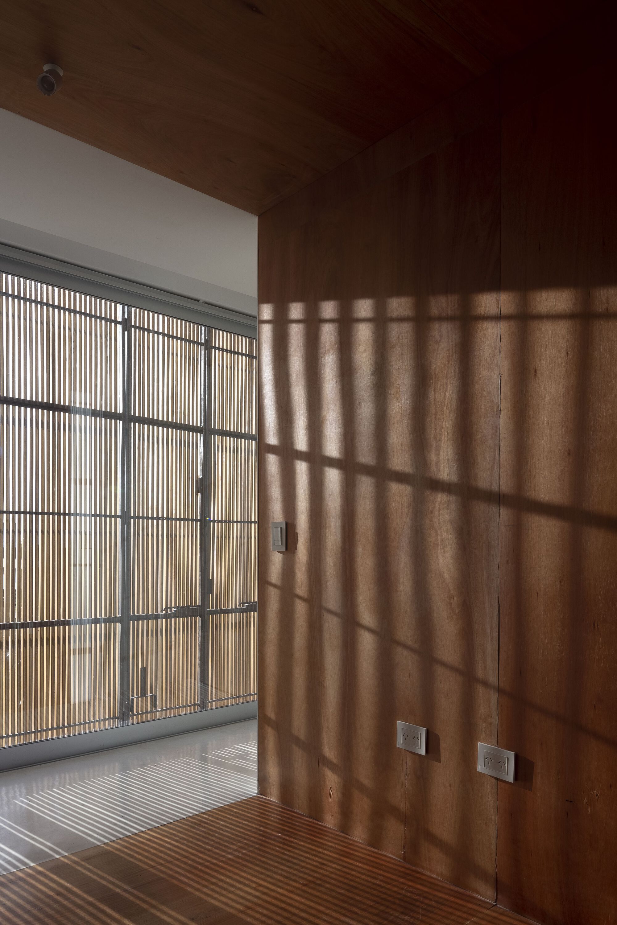 Timber-lined room with slatted screen casting shadow patterns across wall and floor