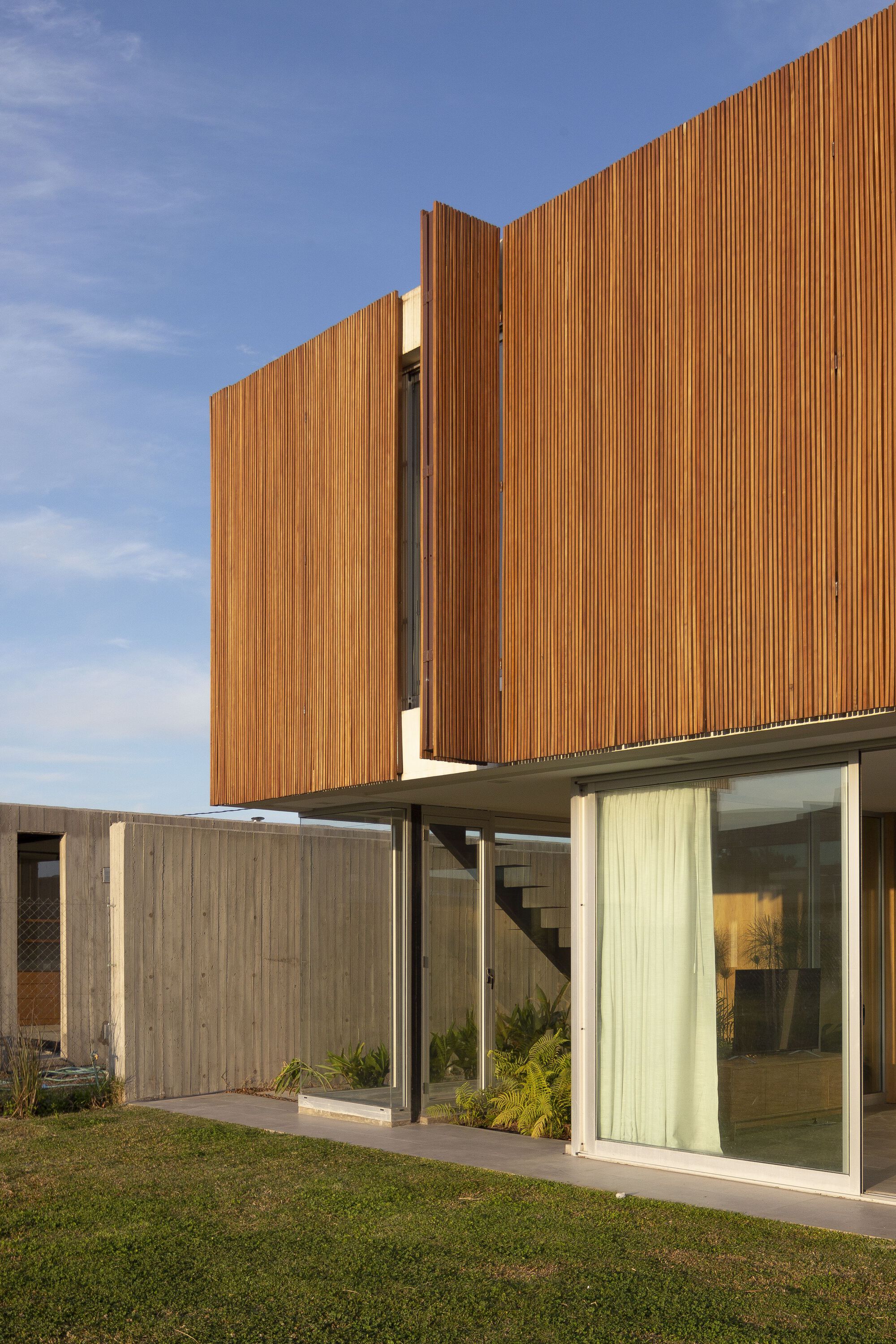 Corner view of cantilevered timber box with recessed glass walls at afternoon light