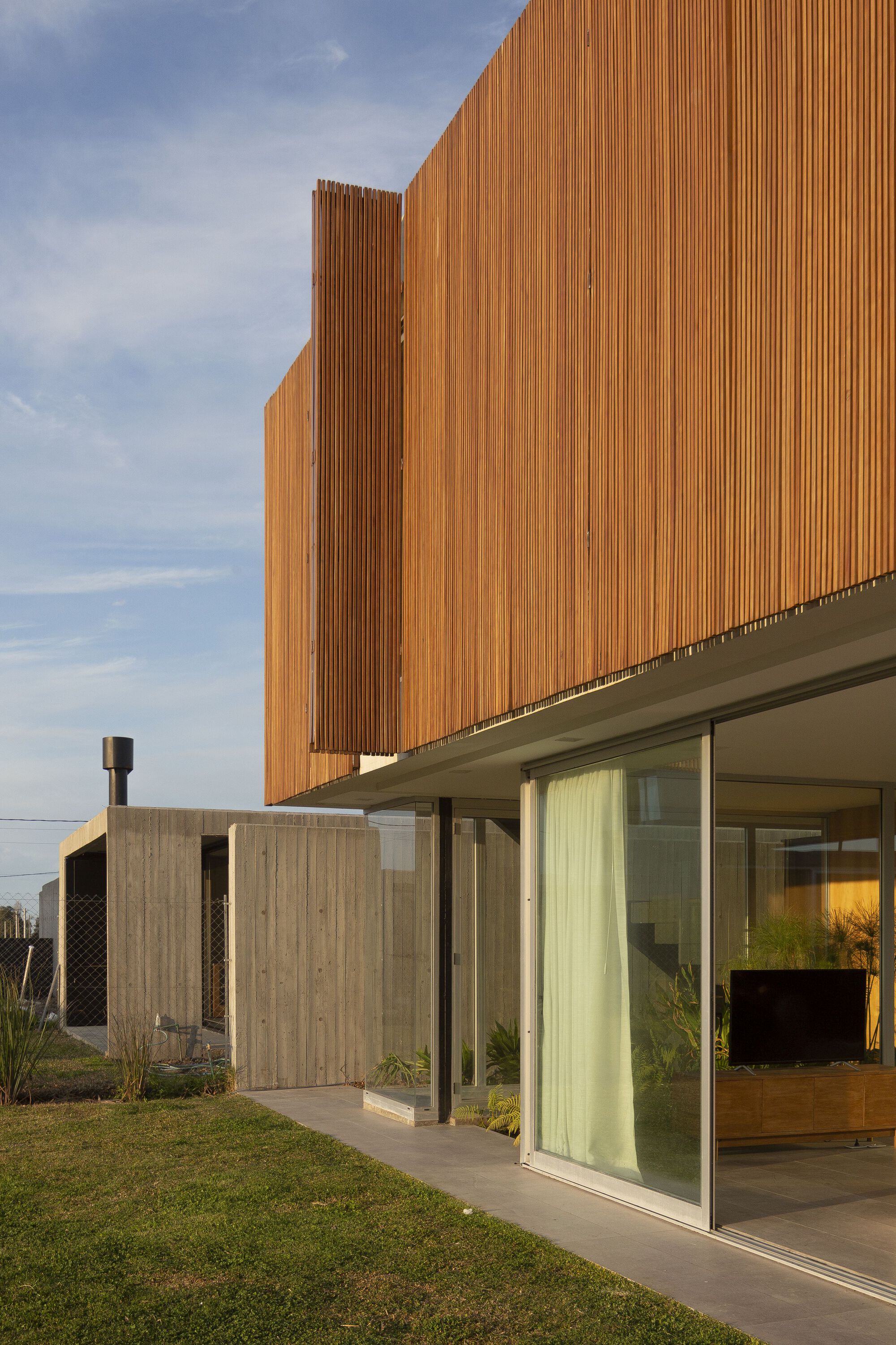 Vertical timber slat facade above glazed walls and grass lawn under a clear blue sky