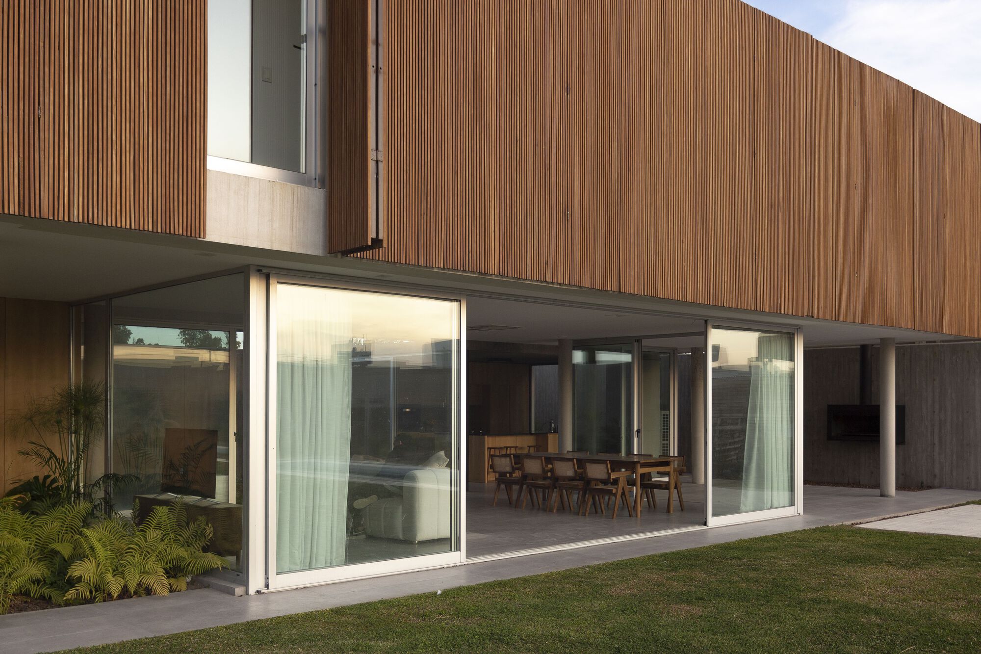 Glazed facade with sliding panels opening to dining area beneath timber clad upper volume