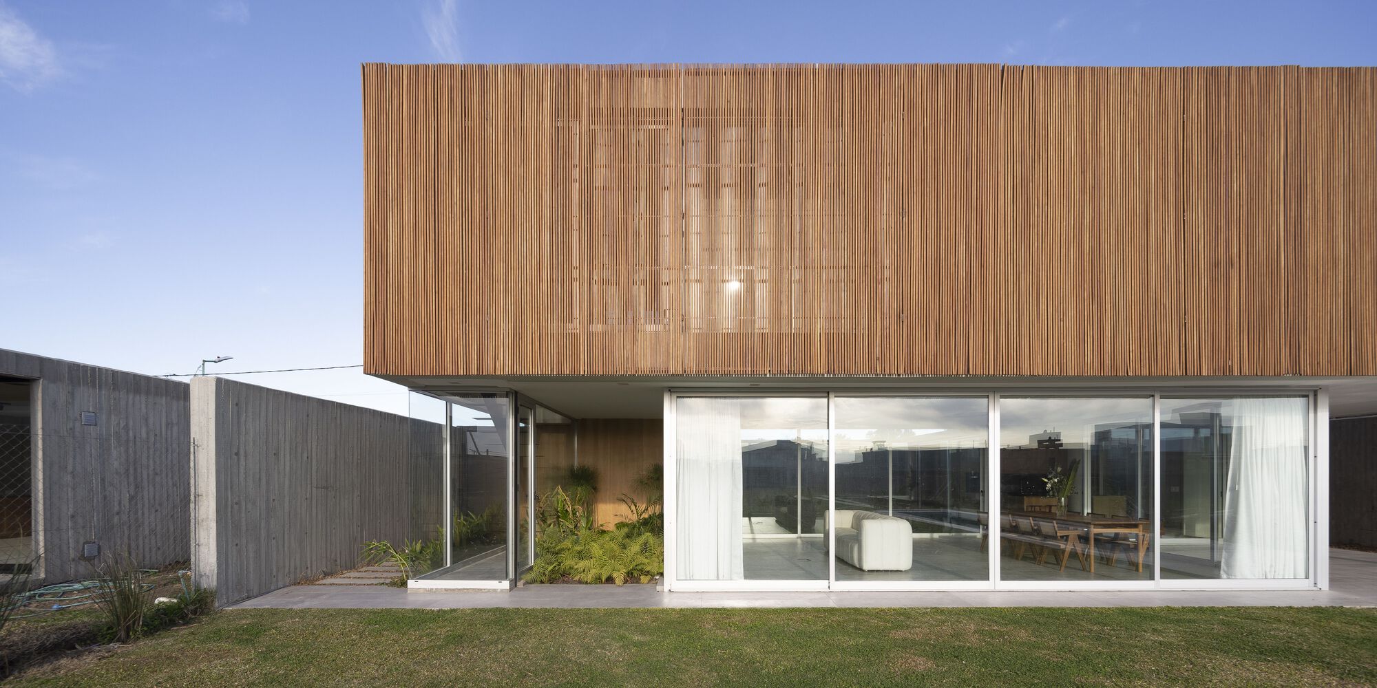 Front elevation showing timber slatted upper floor cantilevered over glazed ground level with lawn