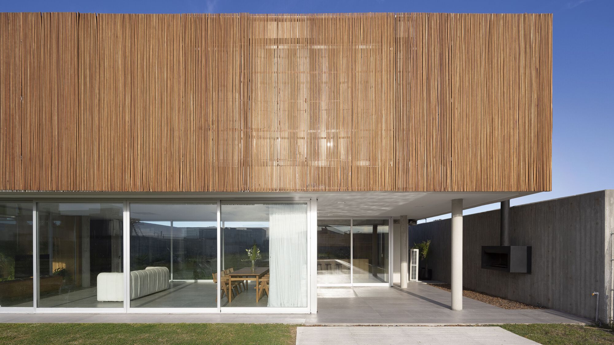 Covered terrace beneath concrete soffit with timber volume above and glass walls opening to interior