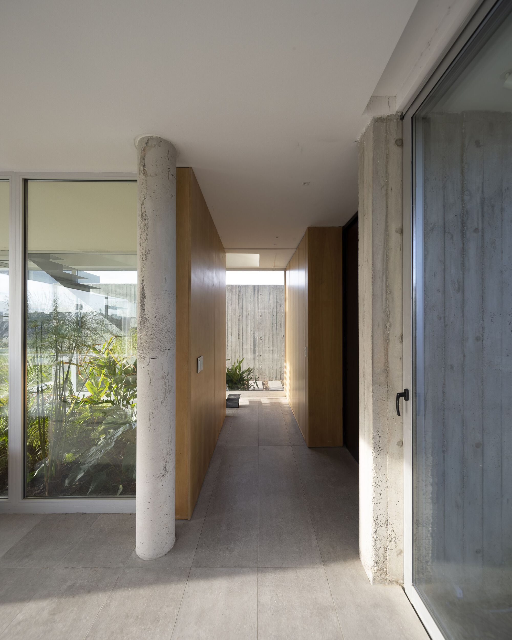 Interior corridor with exposed concrete columns flanked by glazing opening to planted courtyards