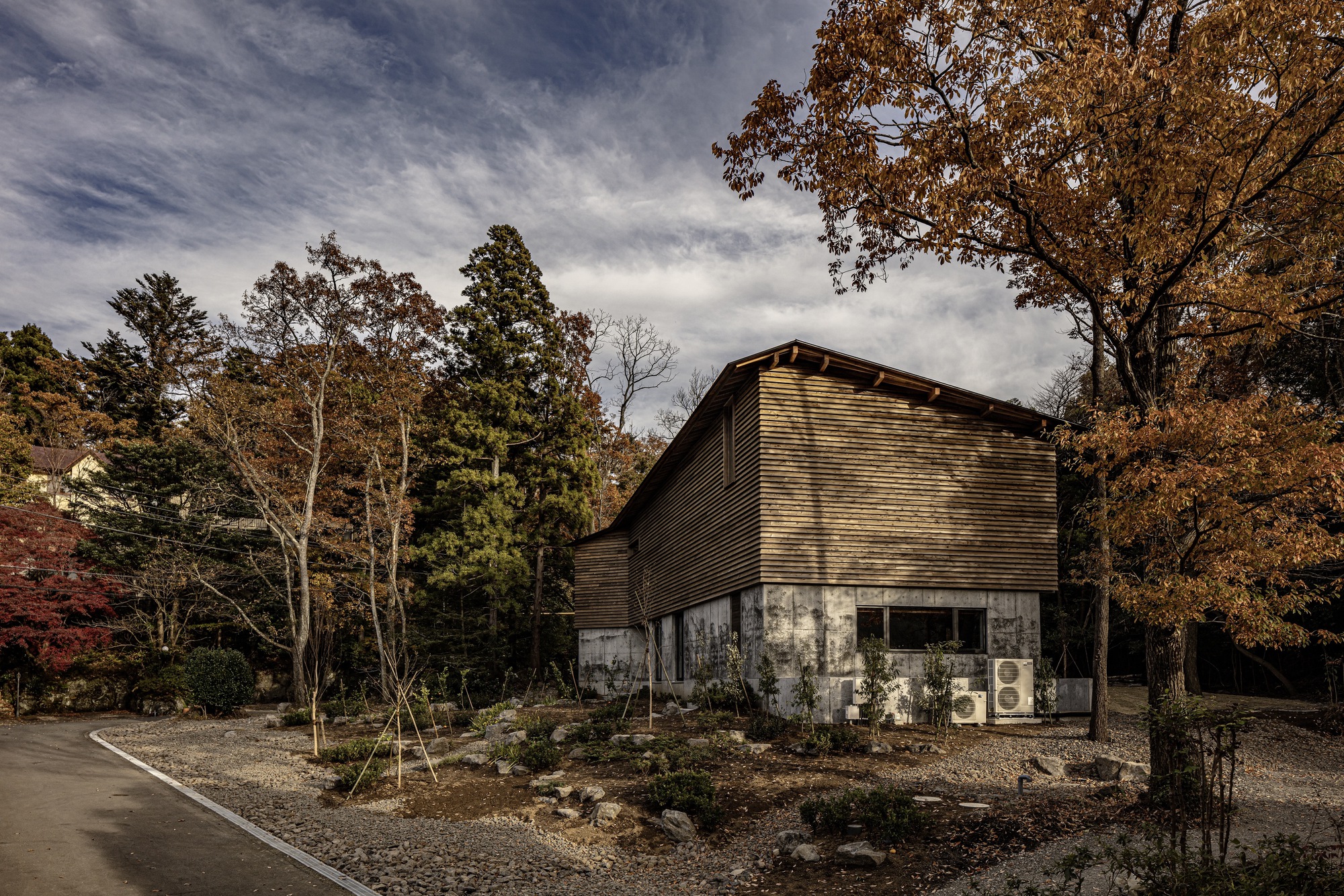 Corner view of the horizontal wood-slatted facade with HVAC units at ground level under autumn foliage