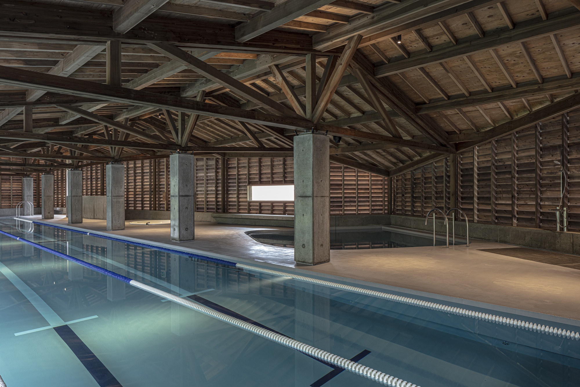 Interior lap pool with exposed timber roof trusses and concrete columns in daylight