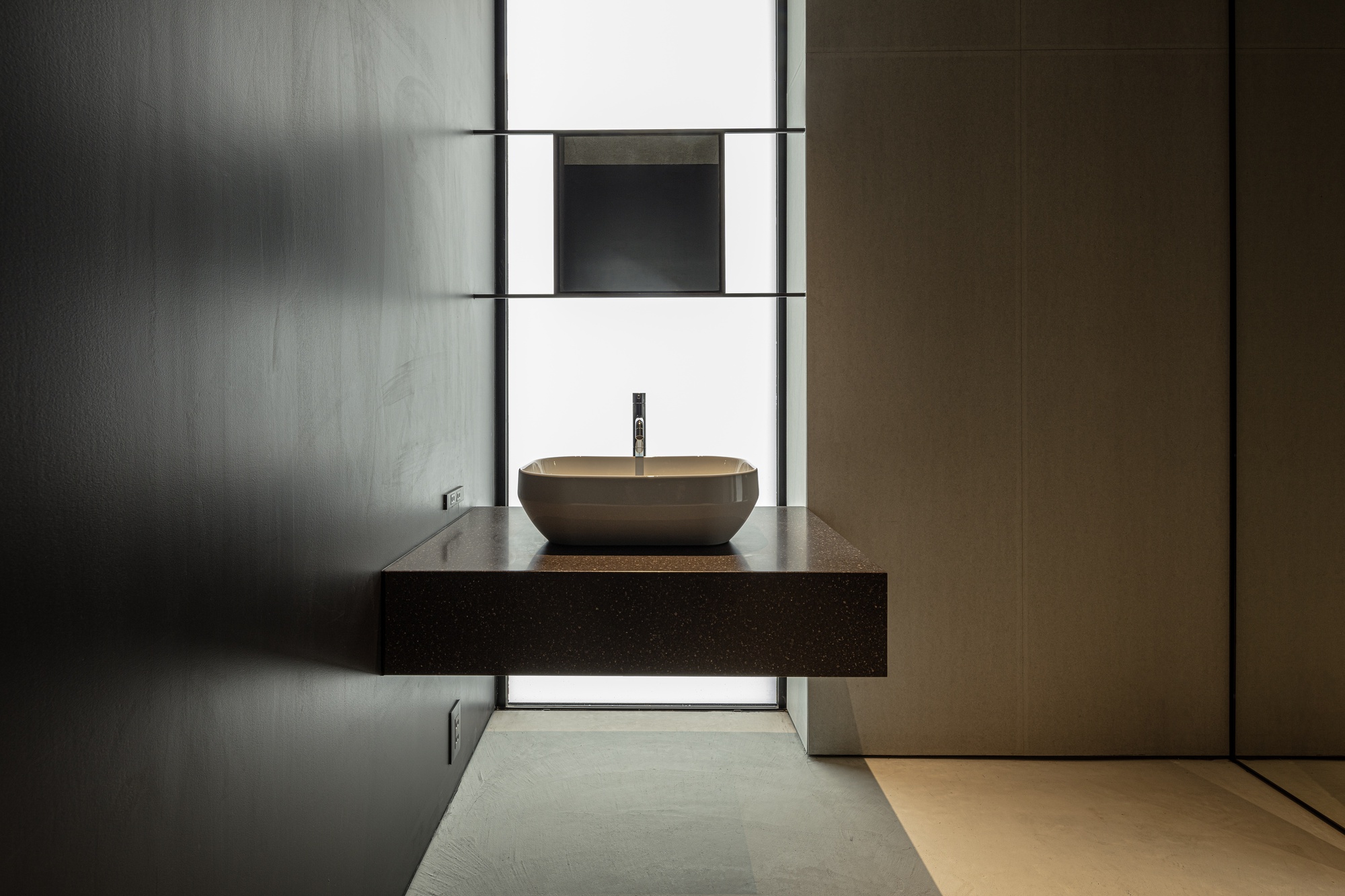Floating vanity with vessel sink beneath a backlit slot window in polished concrete bathroom