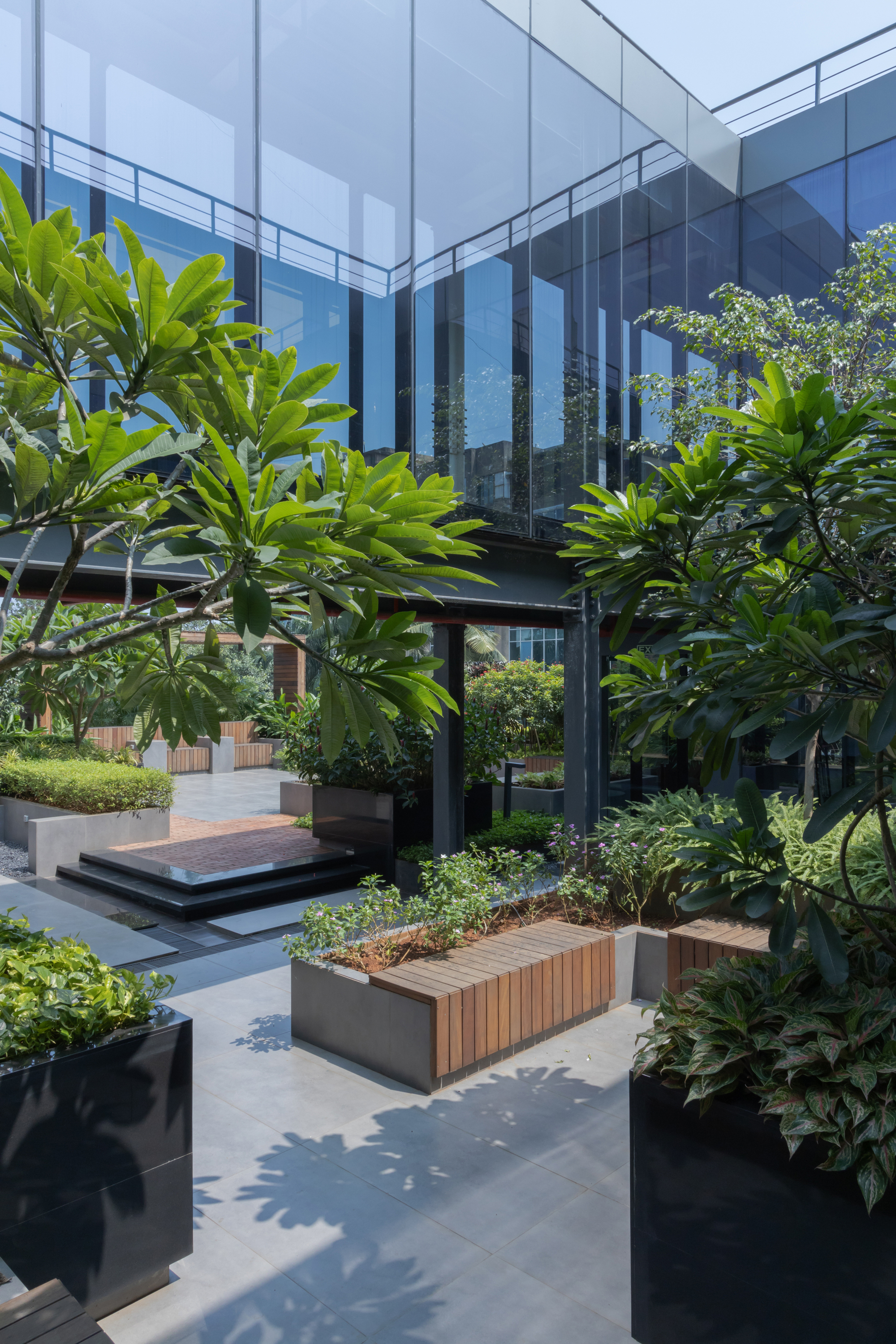 Landscaped courtyard with timber planters and black steel columns beneath the glass bridge