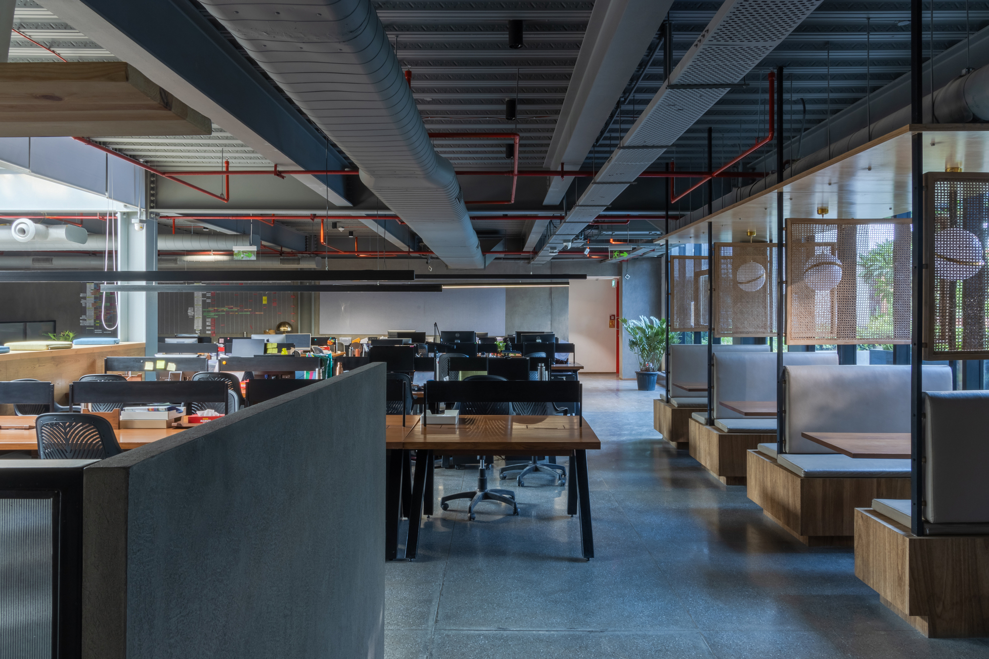 Open-plan office interior with exposed ceiling ducts, workstations and timber booth seating along glazed walls