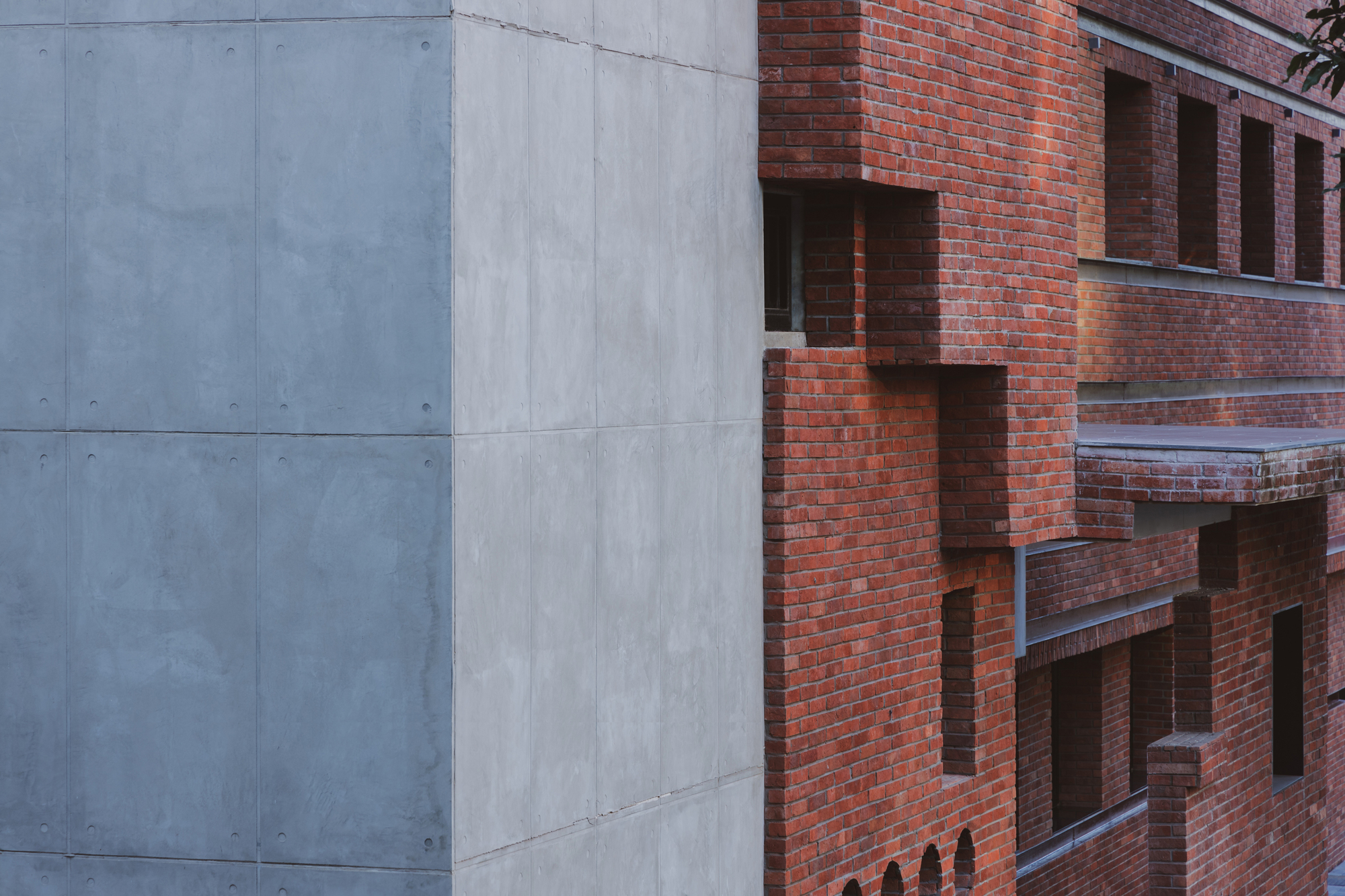 Facade detail showing the junction between smooth concrete panels and textured red brick with recessed openings