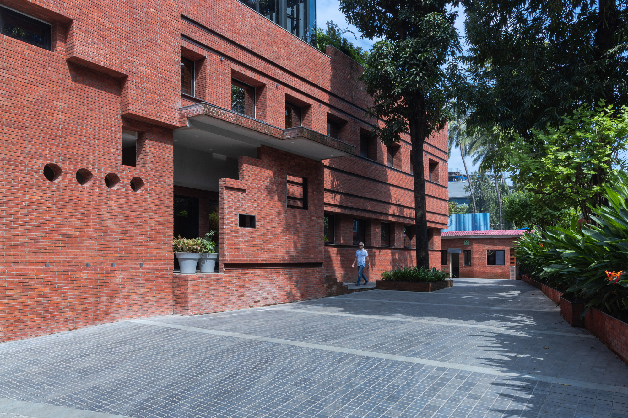 Entry courtyard with red brick facade, covered walkway, and person walking beneath palm trees