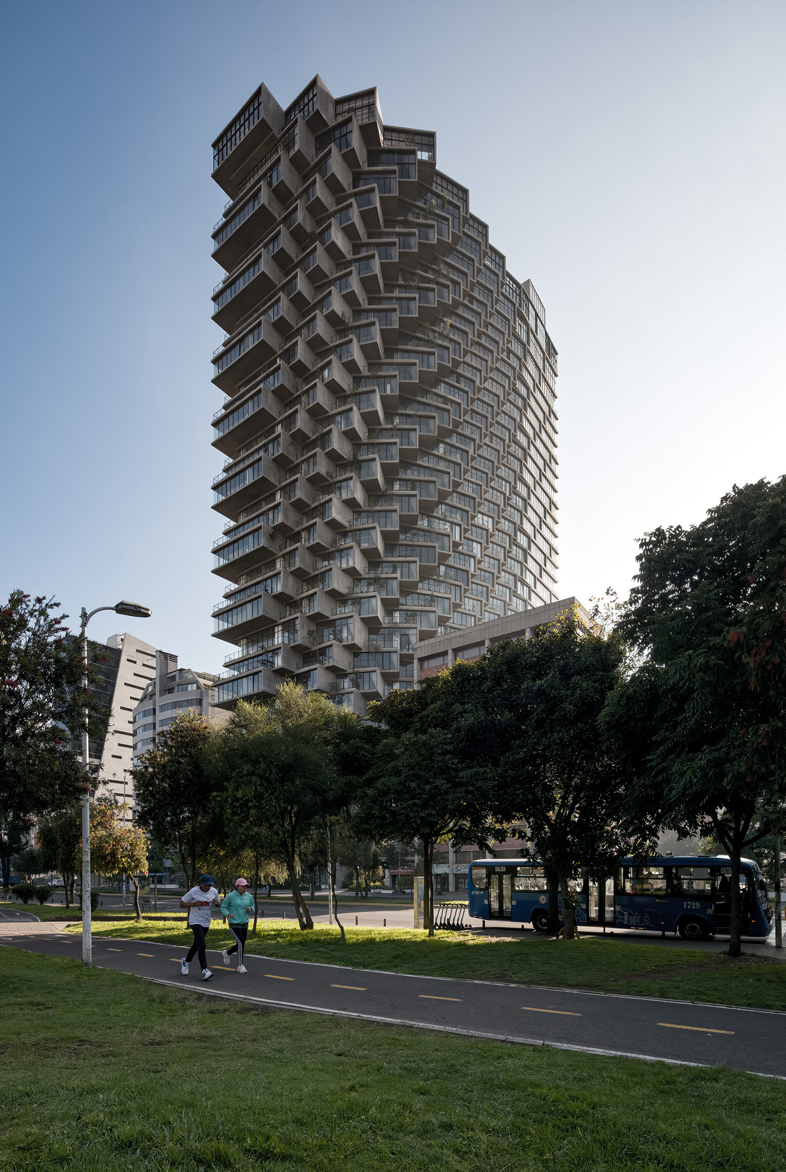 View of the spiraling tower from the park pathway with pedestrians and surrounding trees at dusk