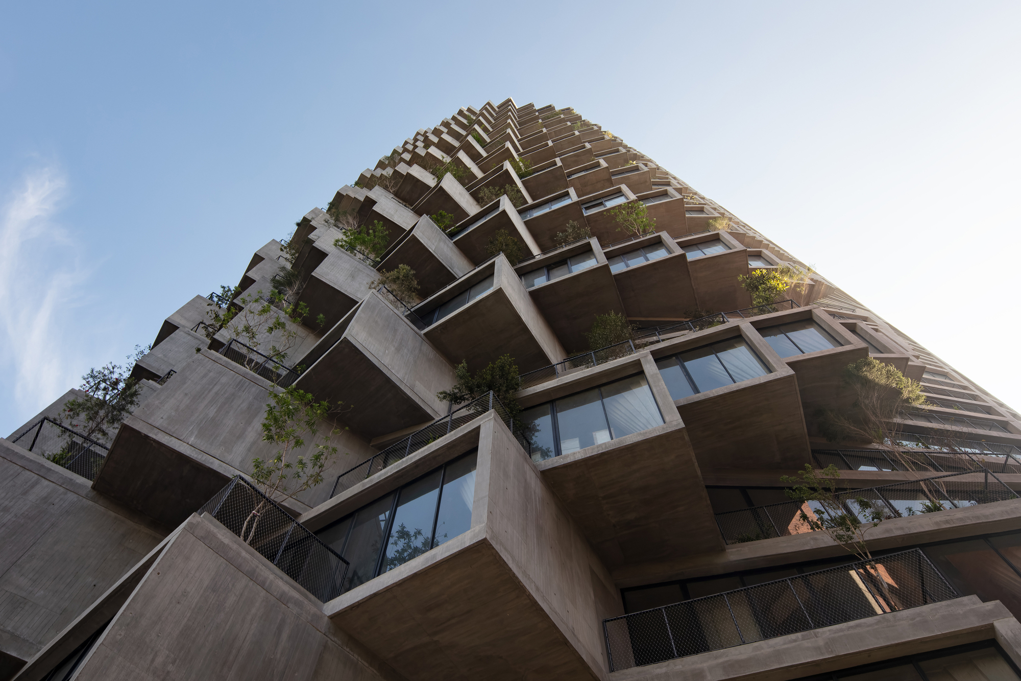 Worm's-eye view of the stacked concrete balconies with planted terraces ascending toward cloudy sky