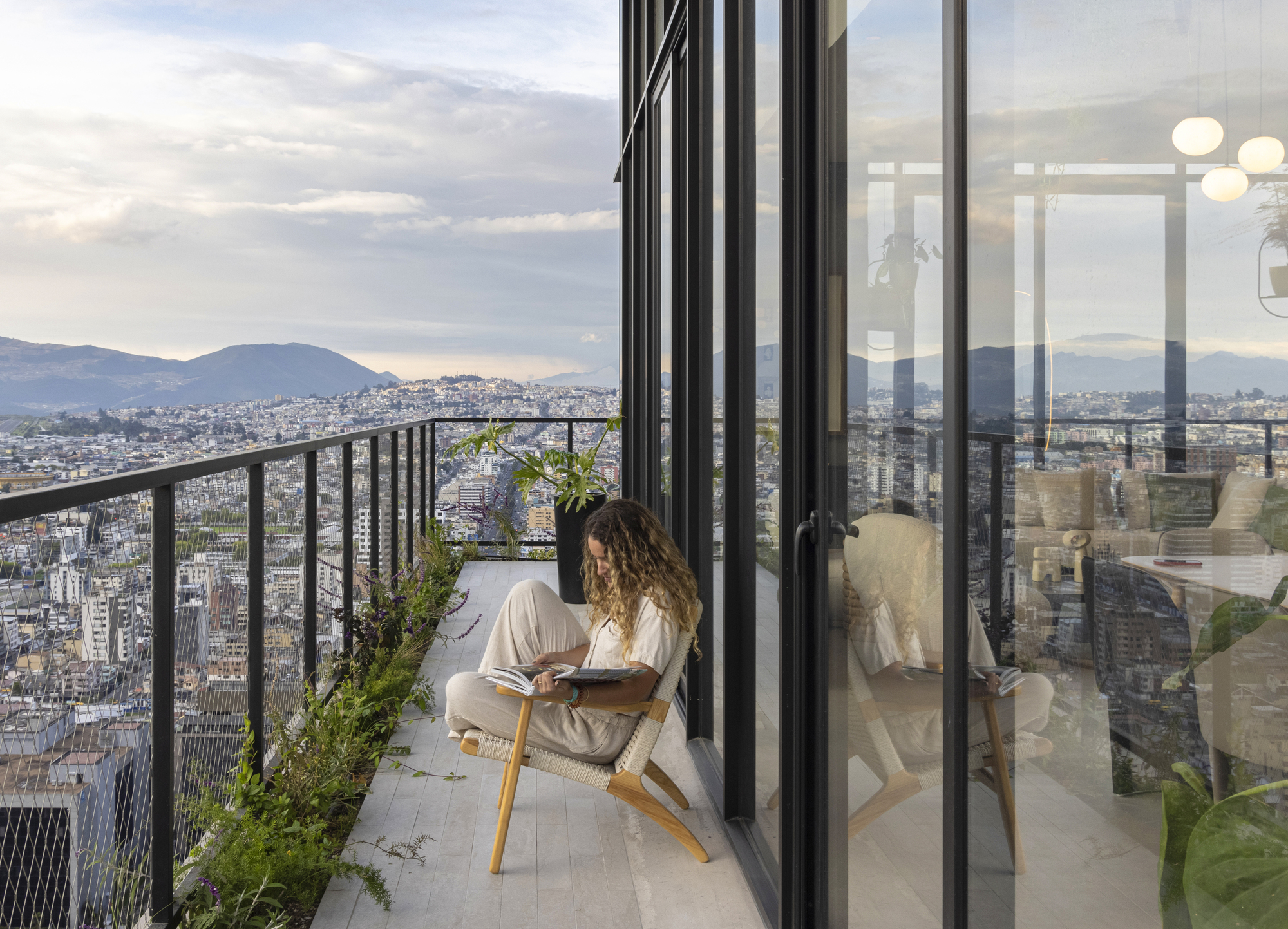 Balcony with metal railing and sliding glass doors overlooking the city at sunset with seated figure