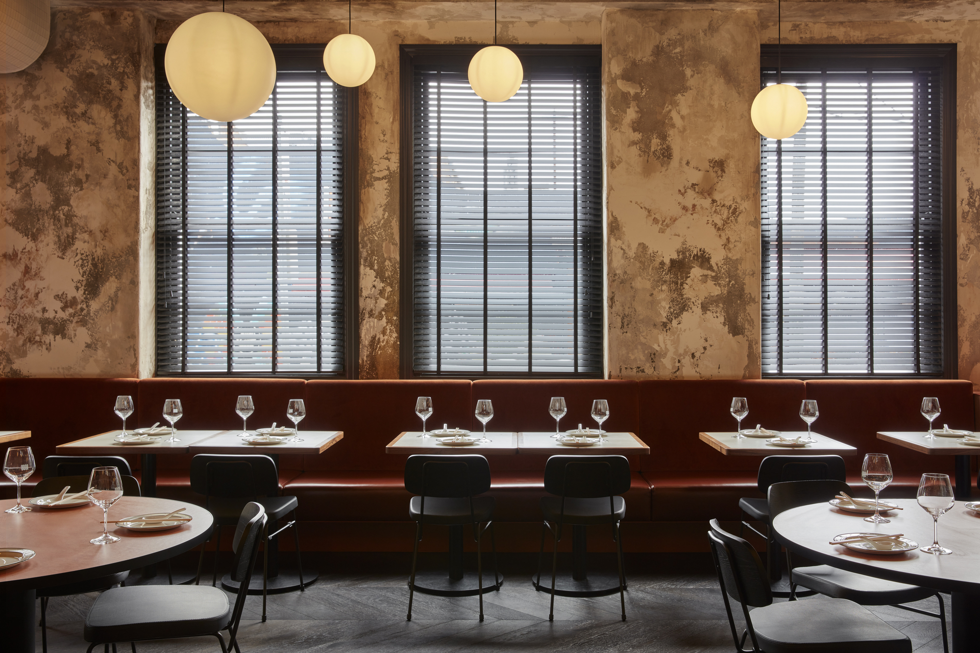 Banquette seating along windows with venetian blinds and sphere pendants above set tables