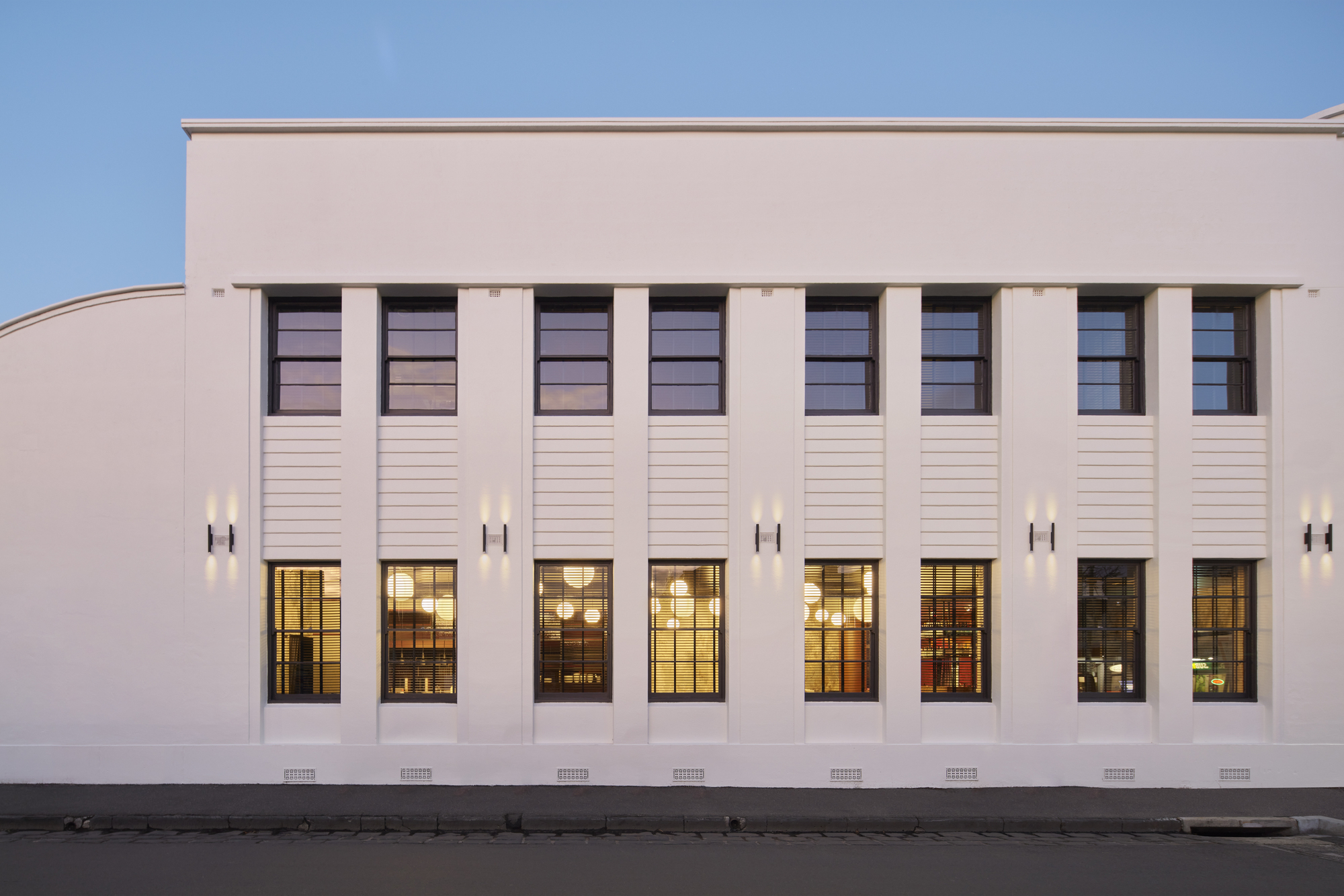 Street facade with vertical pilasters, tall windows, and horizontal louvers under a blue sky