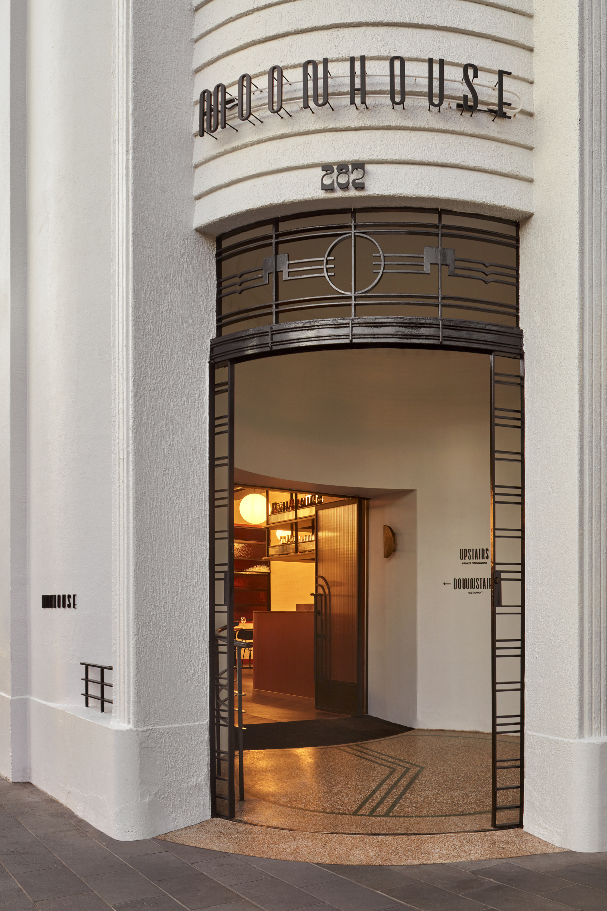 Corner entrance with metal grille surround, curved lettering above, and terrazzo threshold at twilight