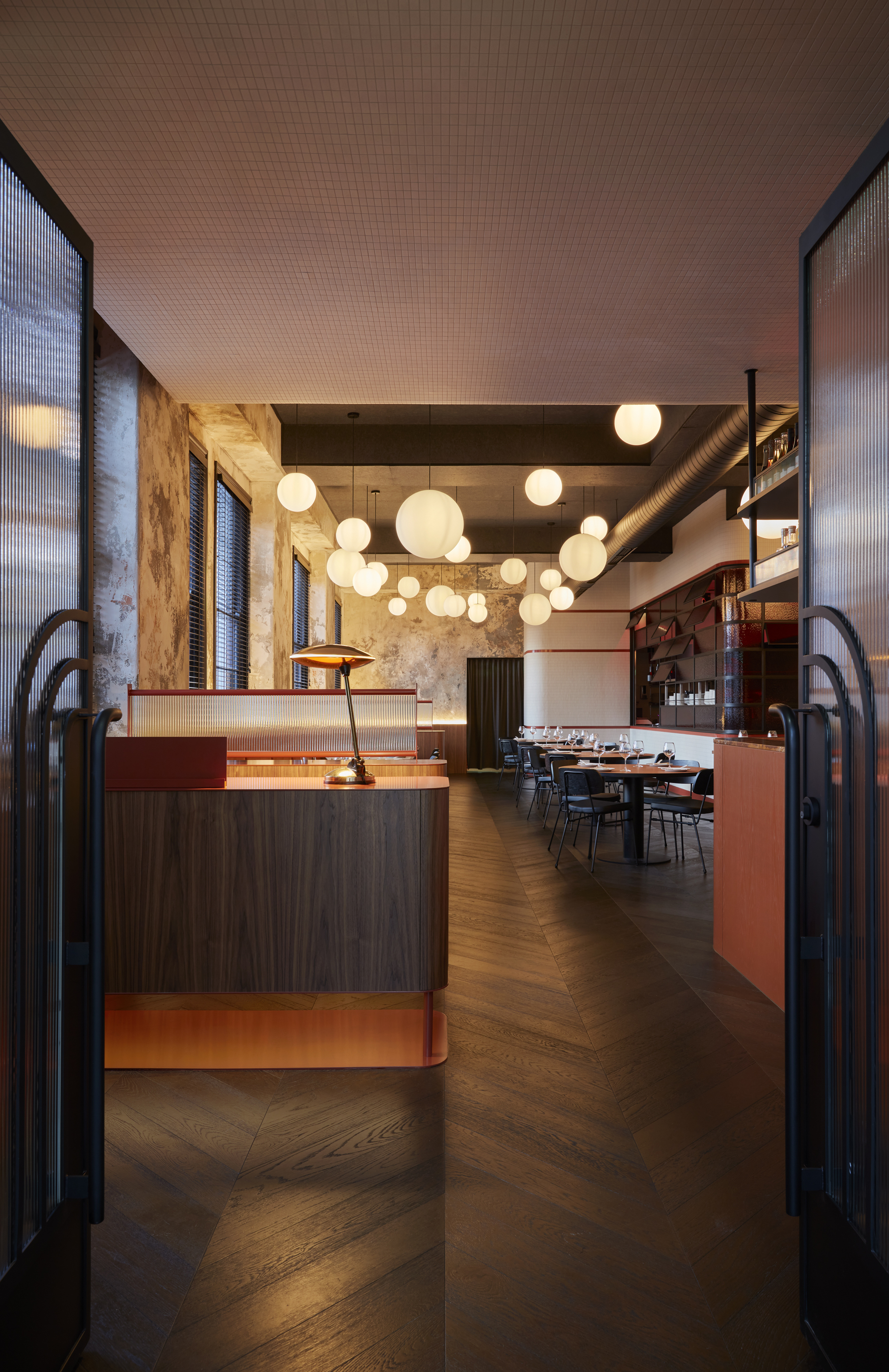 Interior view through arched steel entry doors showing reception desk with globe pendants and herringbone flooring