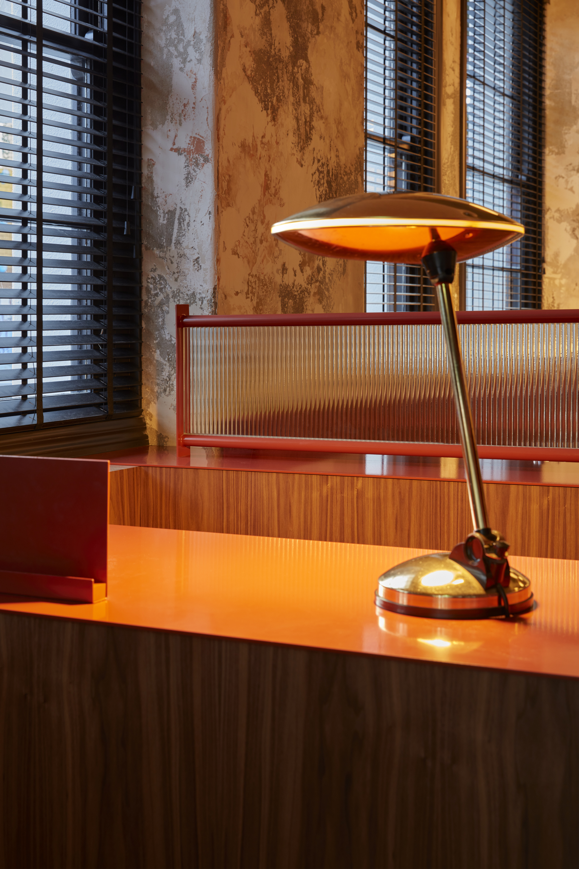 Close-up of brass desk lamp on orange counter with ribbed glass panel and weathered plaster wall